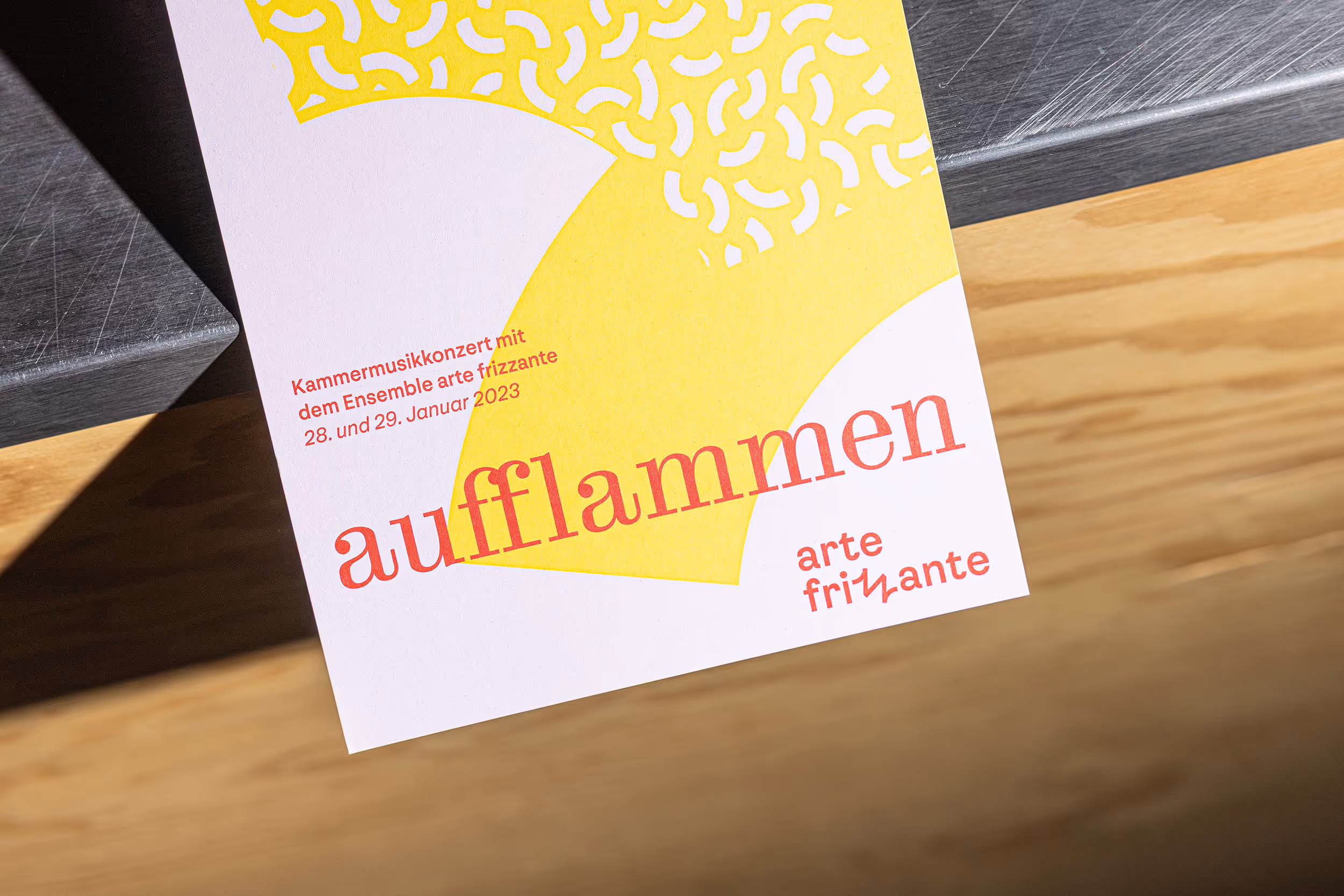 Über eine Kante rangende, farbige Vorderseite eines Konzertflyers für das Orchester arte frizzante