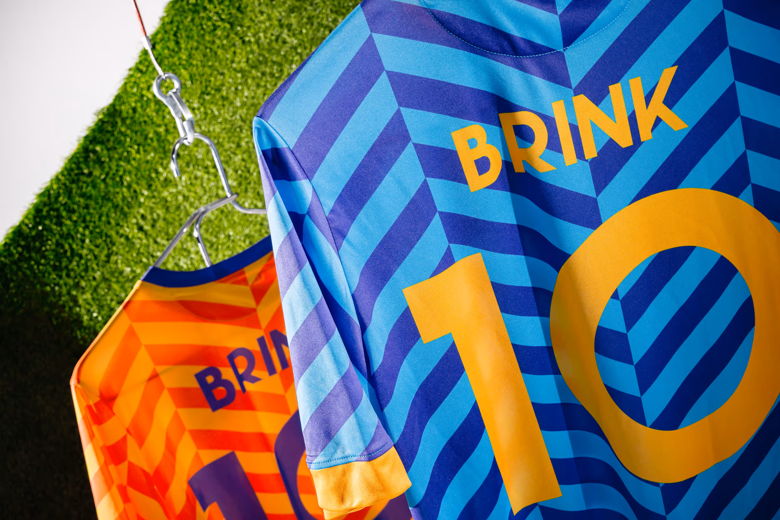 Detailansicht der Trikot-Rückseiten des ObArt Sportvereins, hängend vor einem Stück grünen Kunstrasen