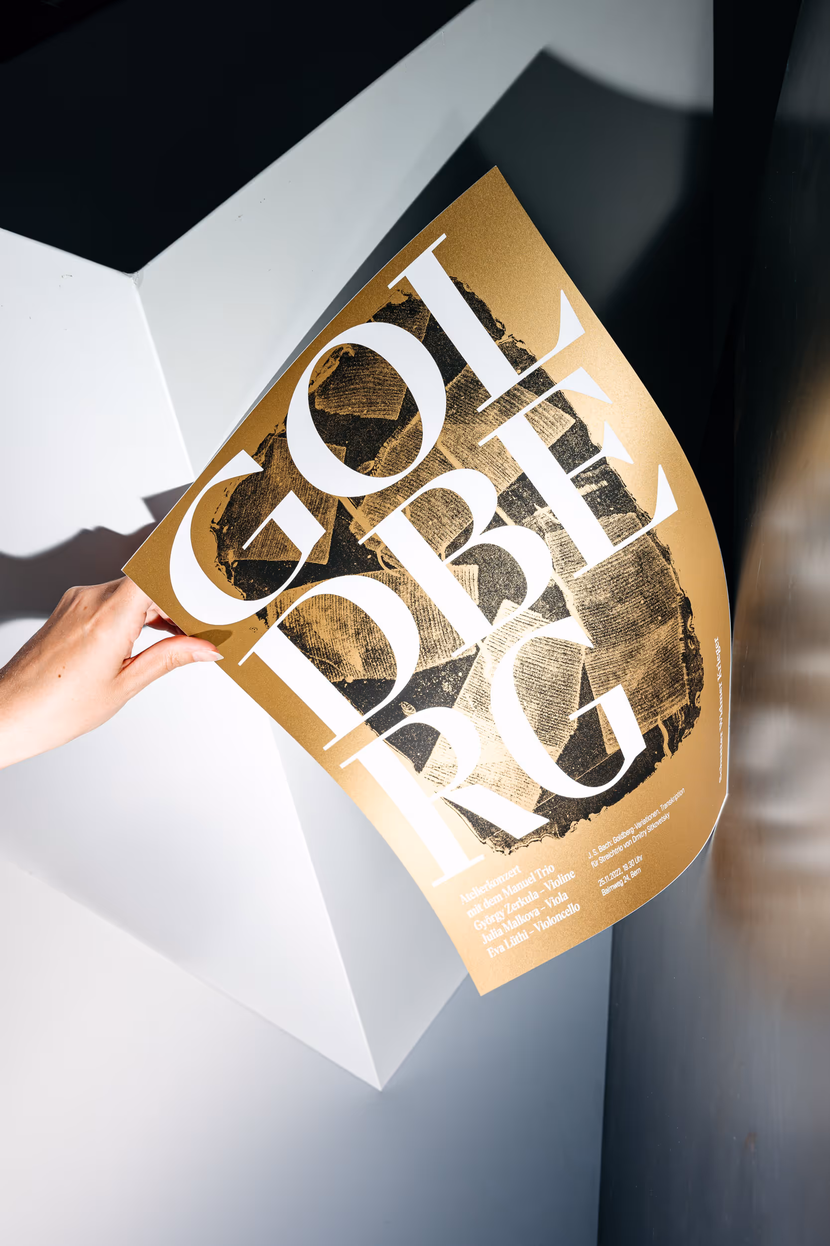 Von einer Hand gehaltenes, gold-farbiges Konzertplakat für das Geigenbauatelier Schutter Widmer