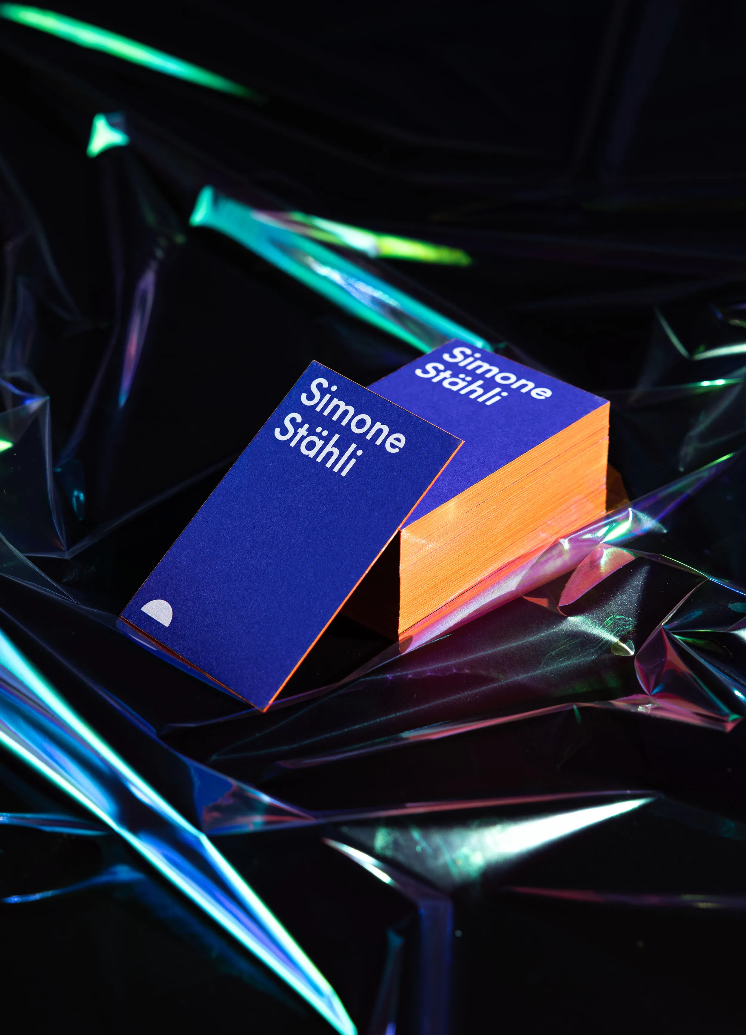 Stapel von leuchtend blauen Visitenkarten mit auffälligem, Neonorange-farbigem Farbschnitt, stehend auf dunklem Untergrund mit leuchtenden Lichtreflexen
