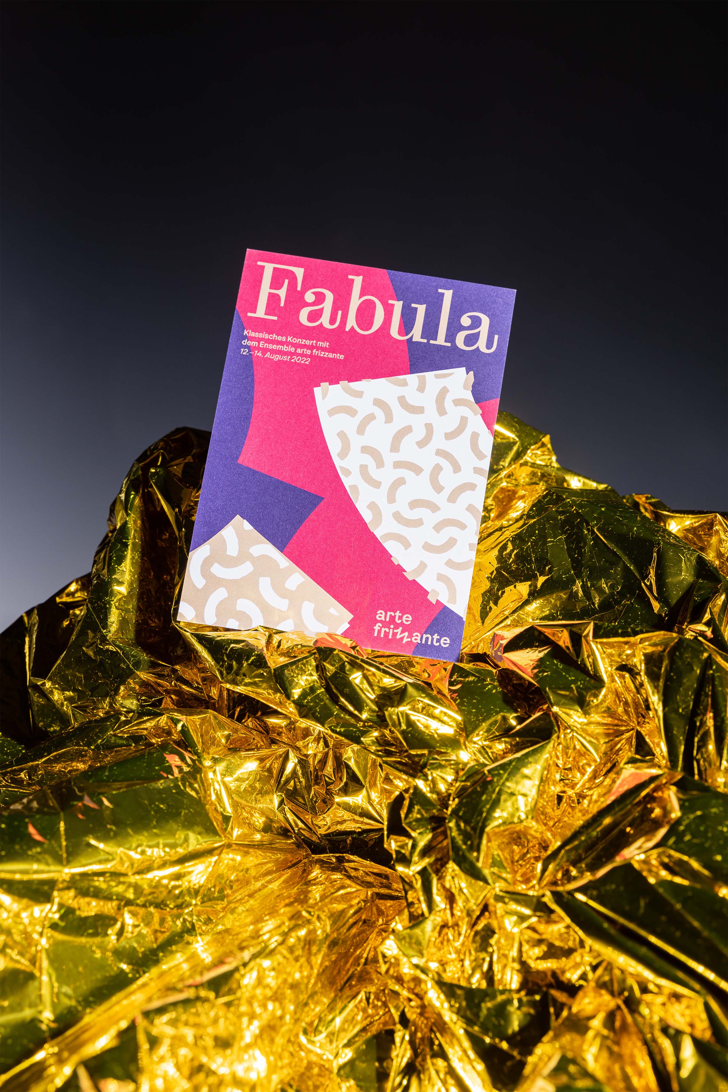 Farbig bedruckte Vorderseite eines Konzertflyers für das Orchester arte frizzante, eingebettet in Goldene Folie vor dunklem Hintergrund