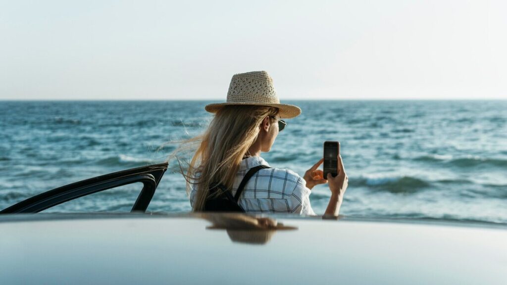 Blonde woman taking a picture by the sea