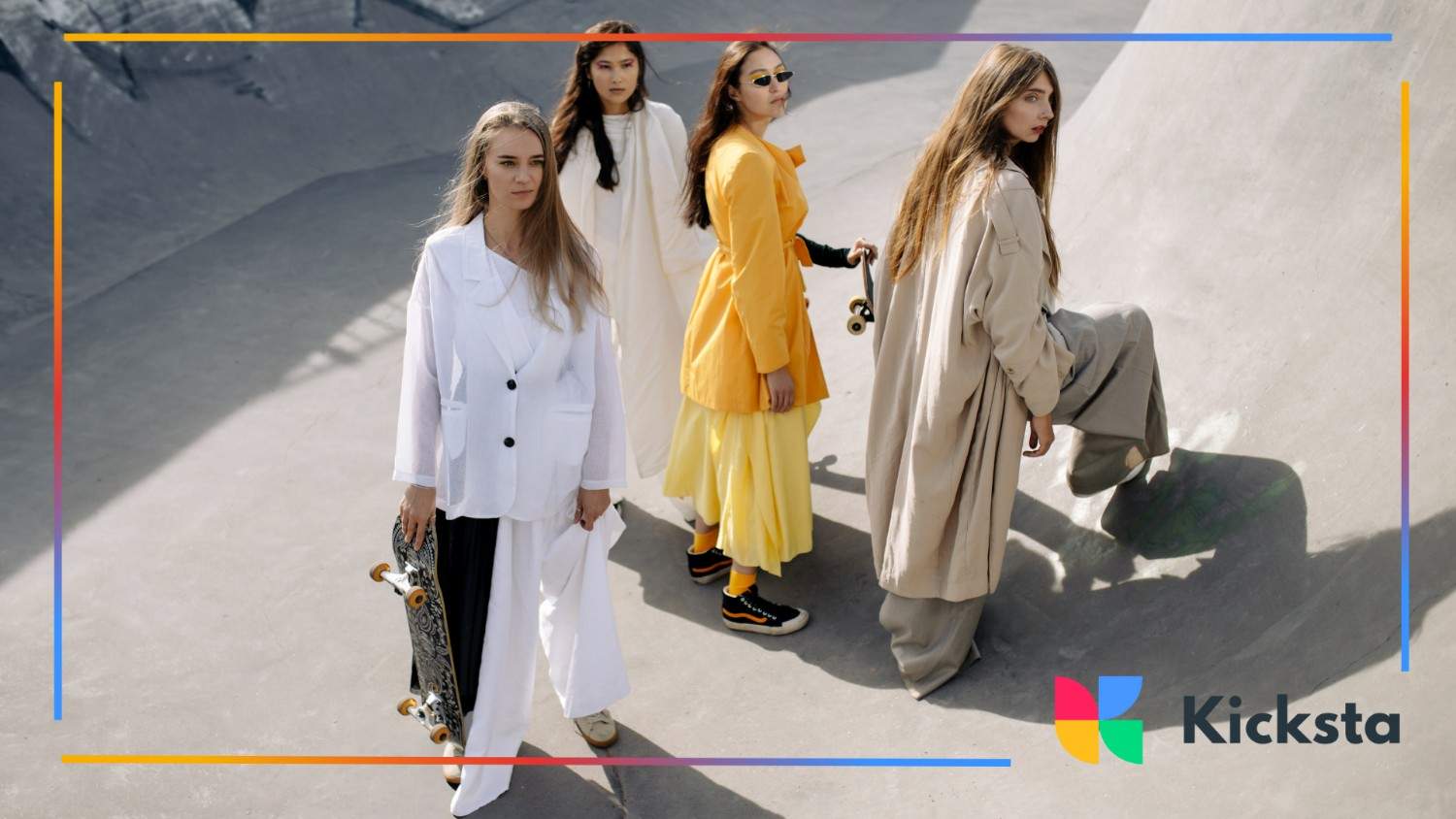 Four fashionable women in layered, modern outfits posing with skateboards in an urban concrete setting