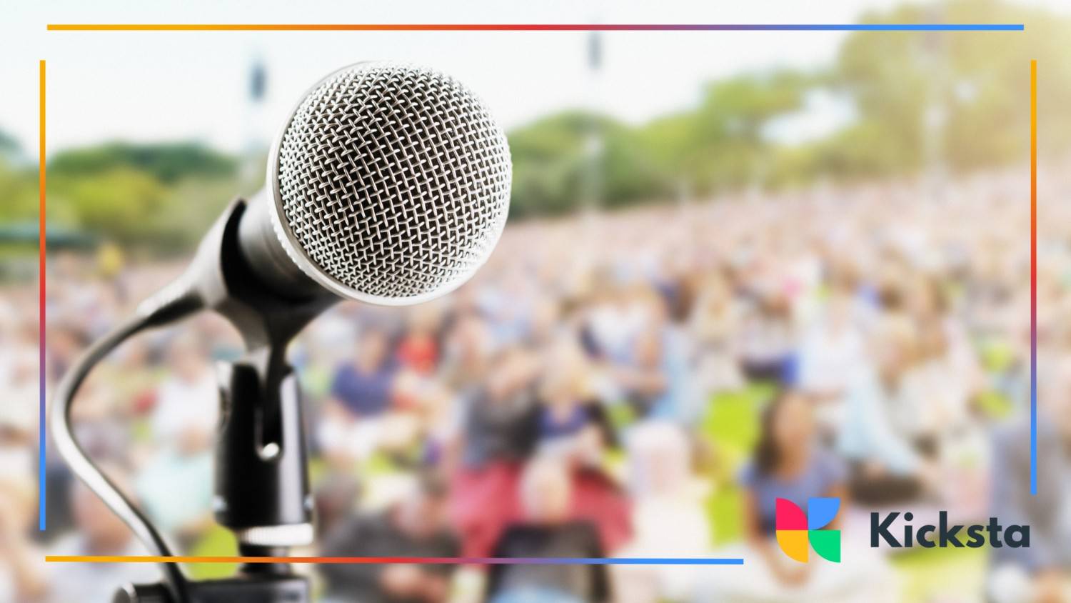 Close-up of a microphone on stage with a large outdoor audience blurred in the background