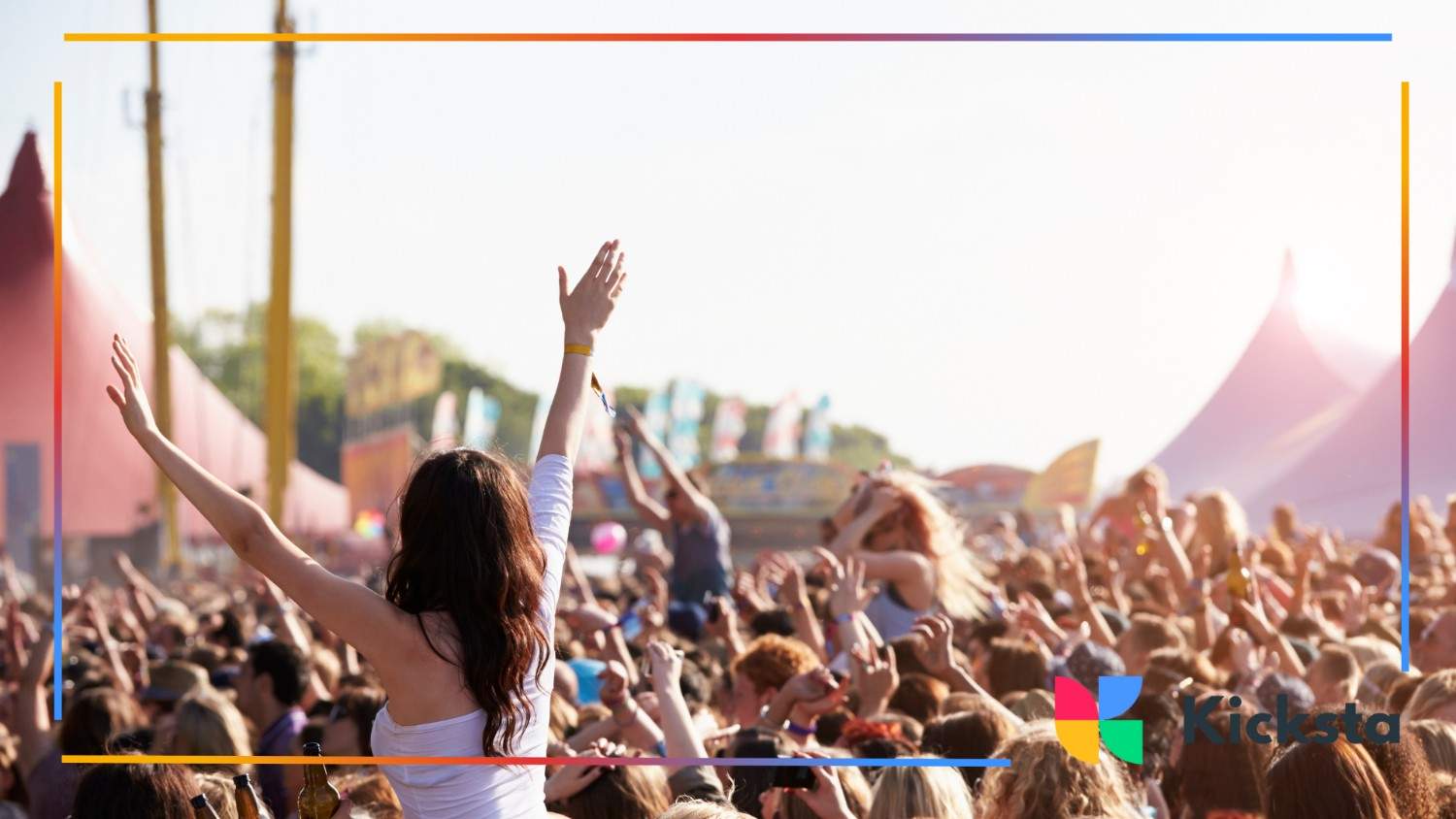 Festival crowd celebrating outdoors under bright sunlight with large colorful tents in the background