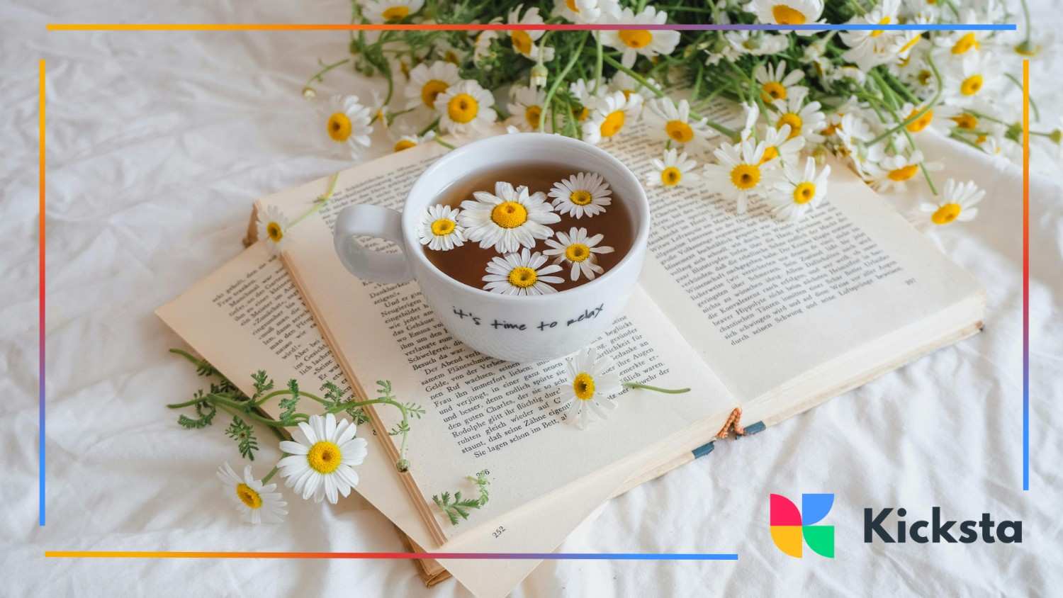 A cup of chamomile tea with floating daisies sits on an open book, surrounded by fresh flowers