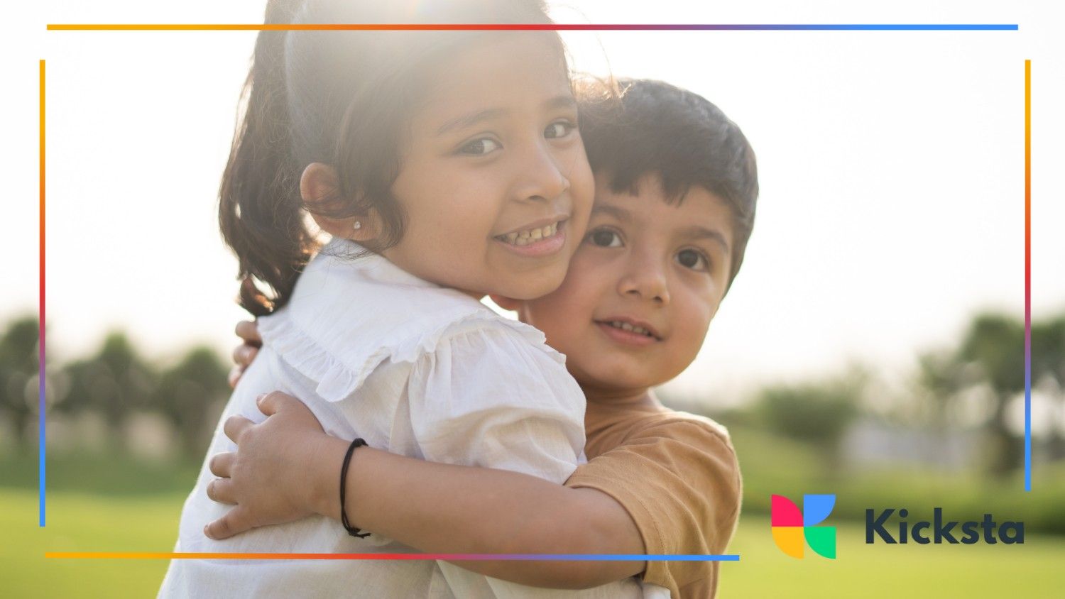 A young girl and boy smiling sweetly as they hug in a sunny park