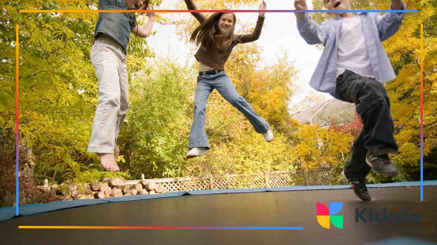 Three children mid-air, joyfully jumping on a trampoline surrounded by autumn trees