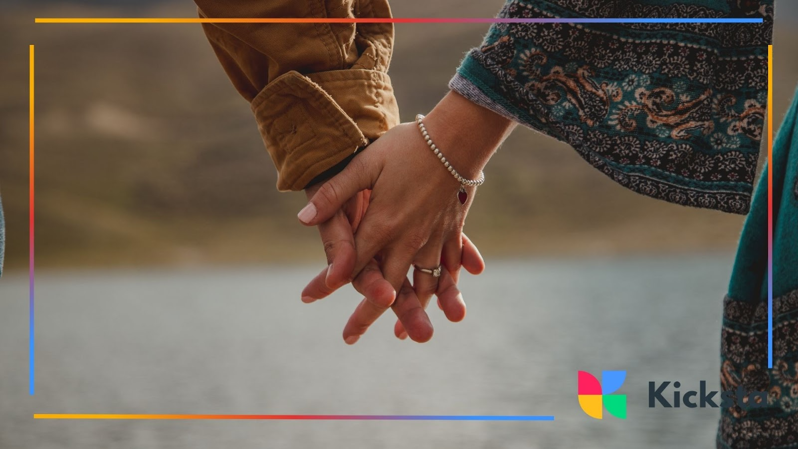 A couple gently holds hands, their fingers intertwined in a quiet moment of connection and affection by the water