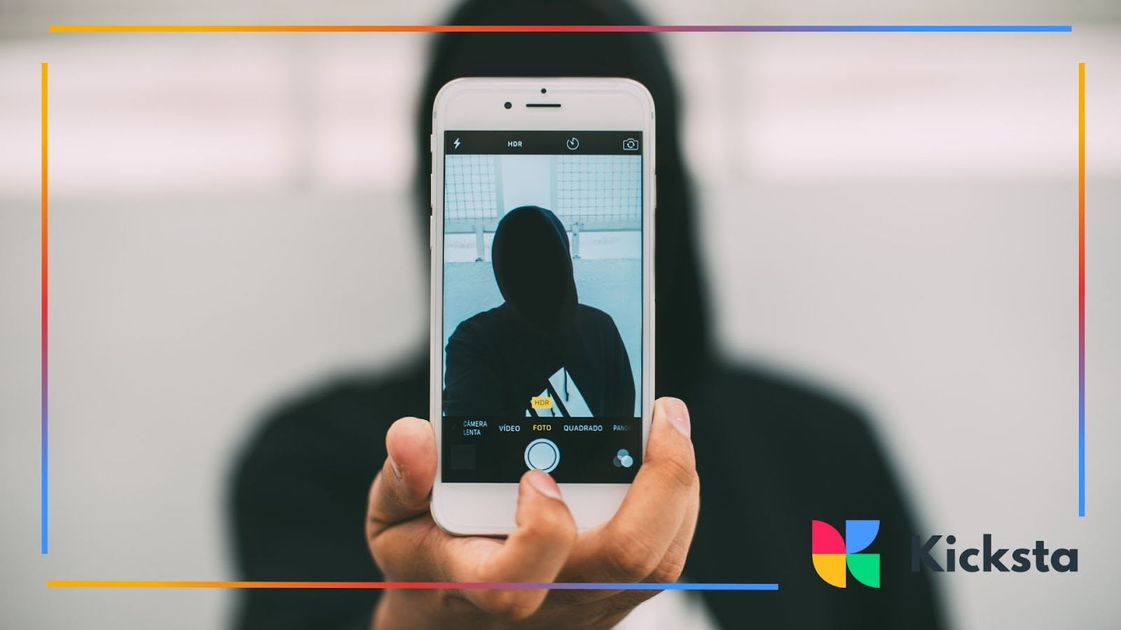 A person in a hoodie holding a smartphone in front of their face, creating a mysterious or anonymous effect.