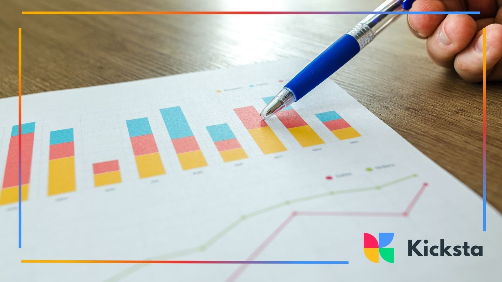 A hand holding a pen pointing at a colorful bar chart on paper, showing financial or business analysis.
