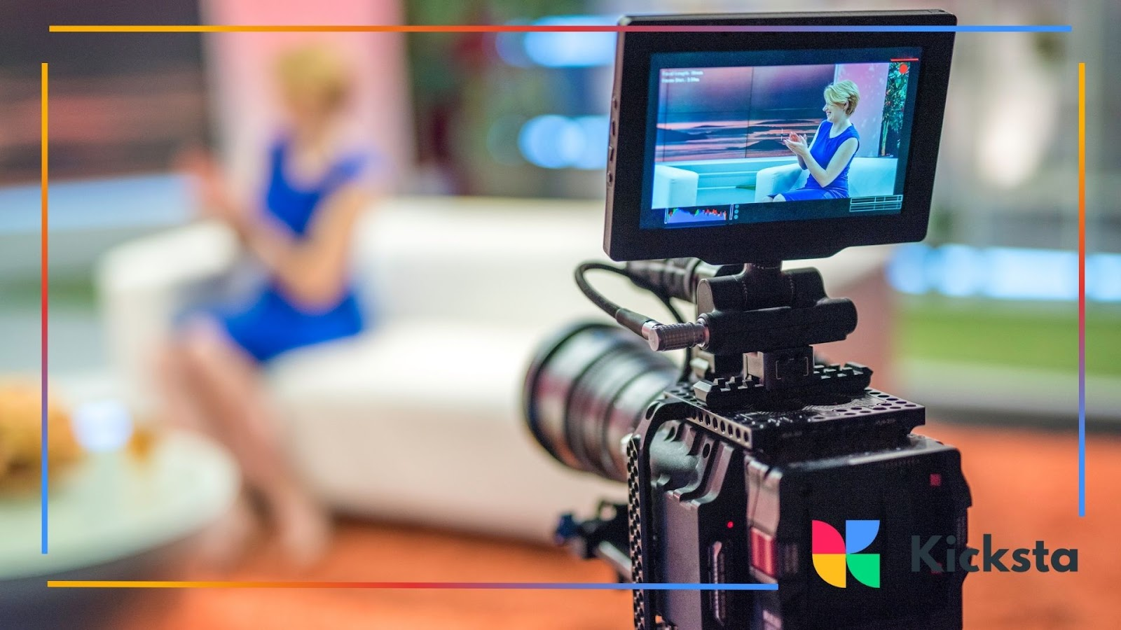Professional video camera recording a woman in a blue dress sitting on a couch in a studio.