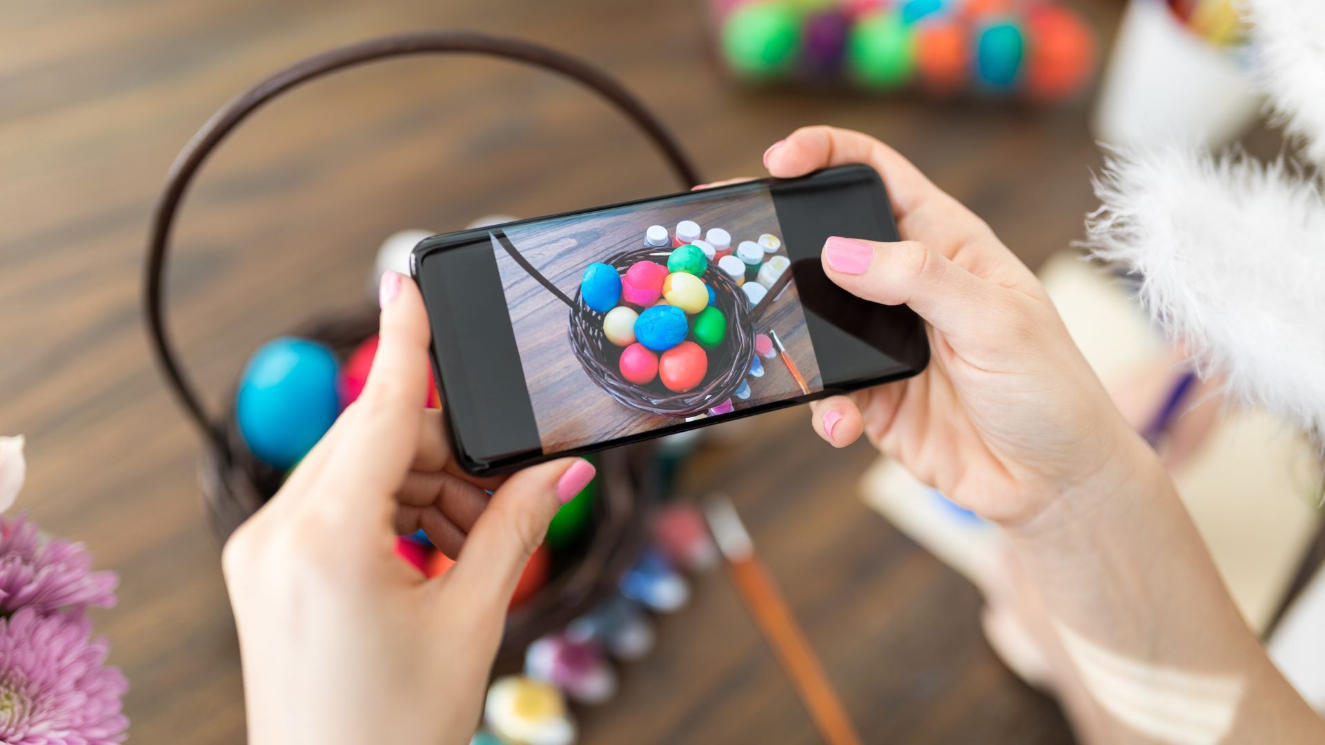 Person photographing a basket of colorful Easter eggs with a smartphone