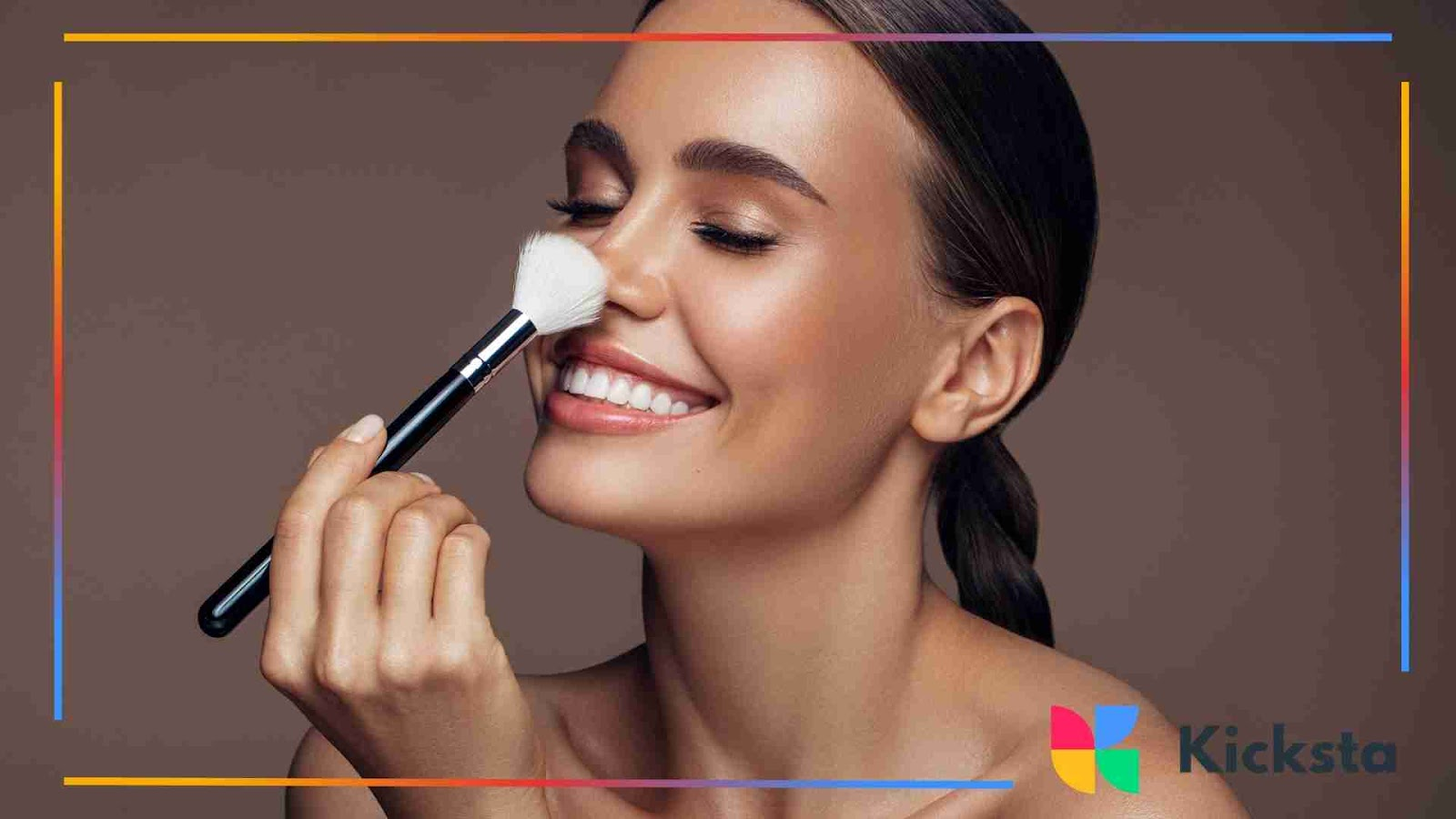 Smiling woman playfully holding a makeup brush to her nose.