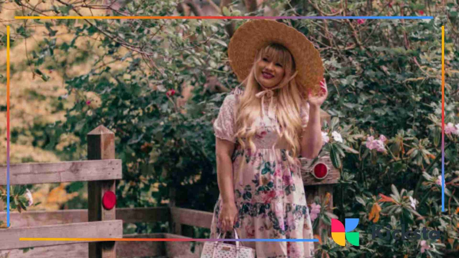 Woman in floral dress and wide-brim hat posing outdoors in a garden setting showcasing cottagecore aesthetic.