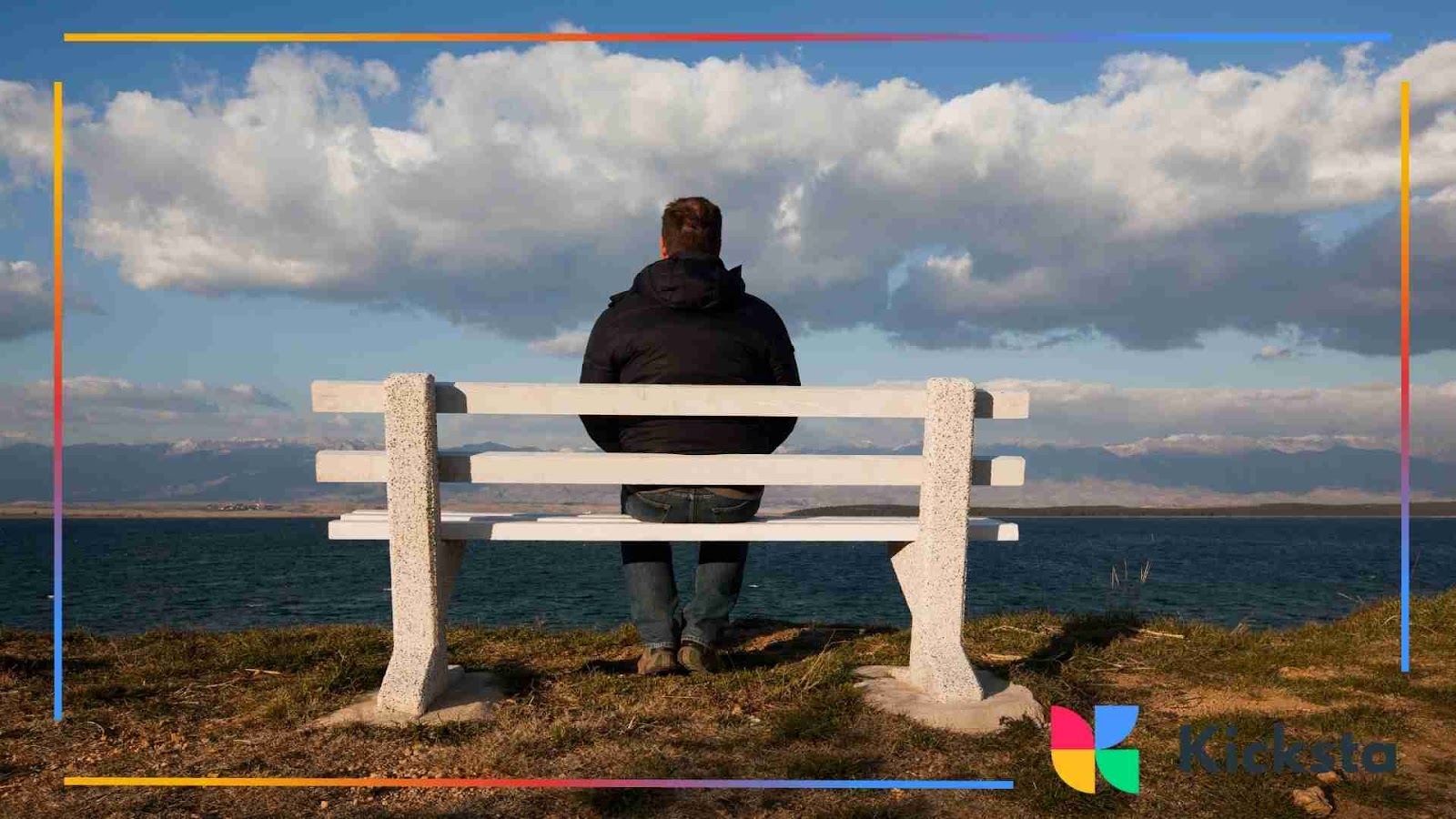 A man sitting solo on a white bench, gazing out over the water under a cloudy sky, sad and lonely