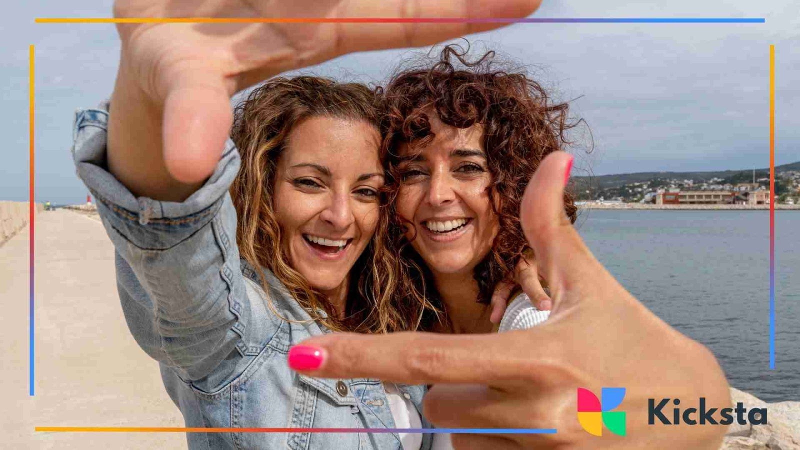 Two curly-haired women smiling and posing together at the beach