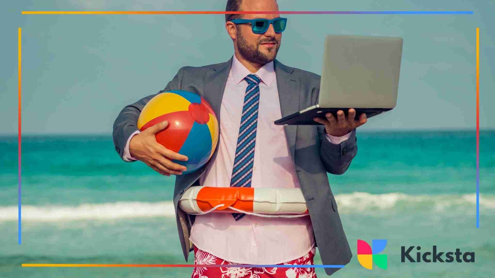 Man in a suit and tie holding a laptop and beach ball at the ocean, mixing work and vacation.