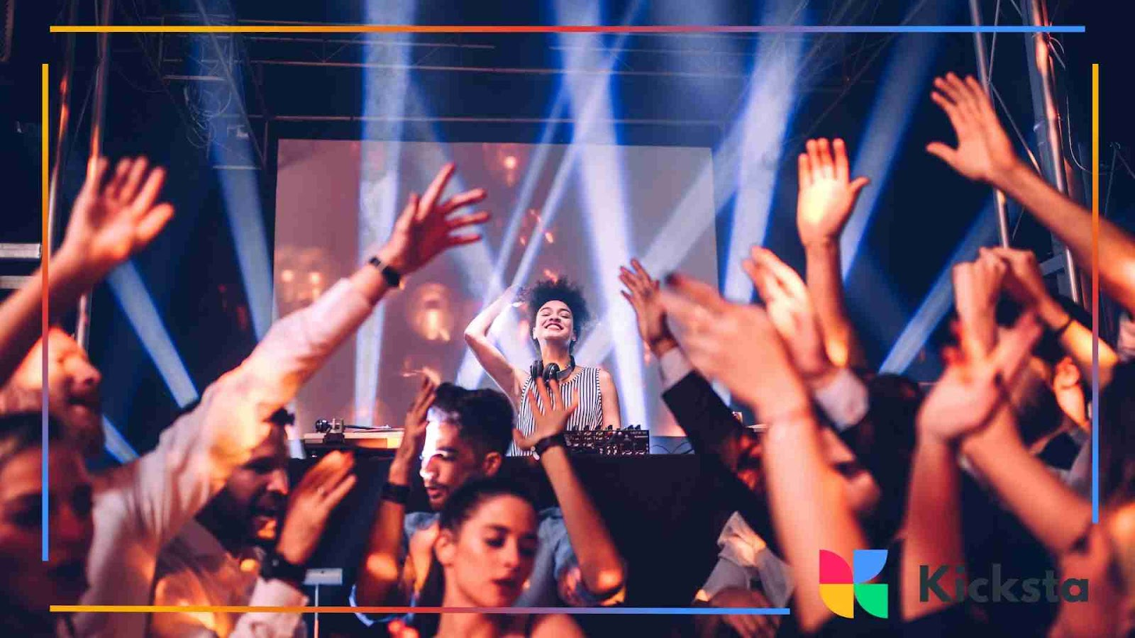 Crowded nightclub with people dancing under bright stage lights and a DJ performing.
