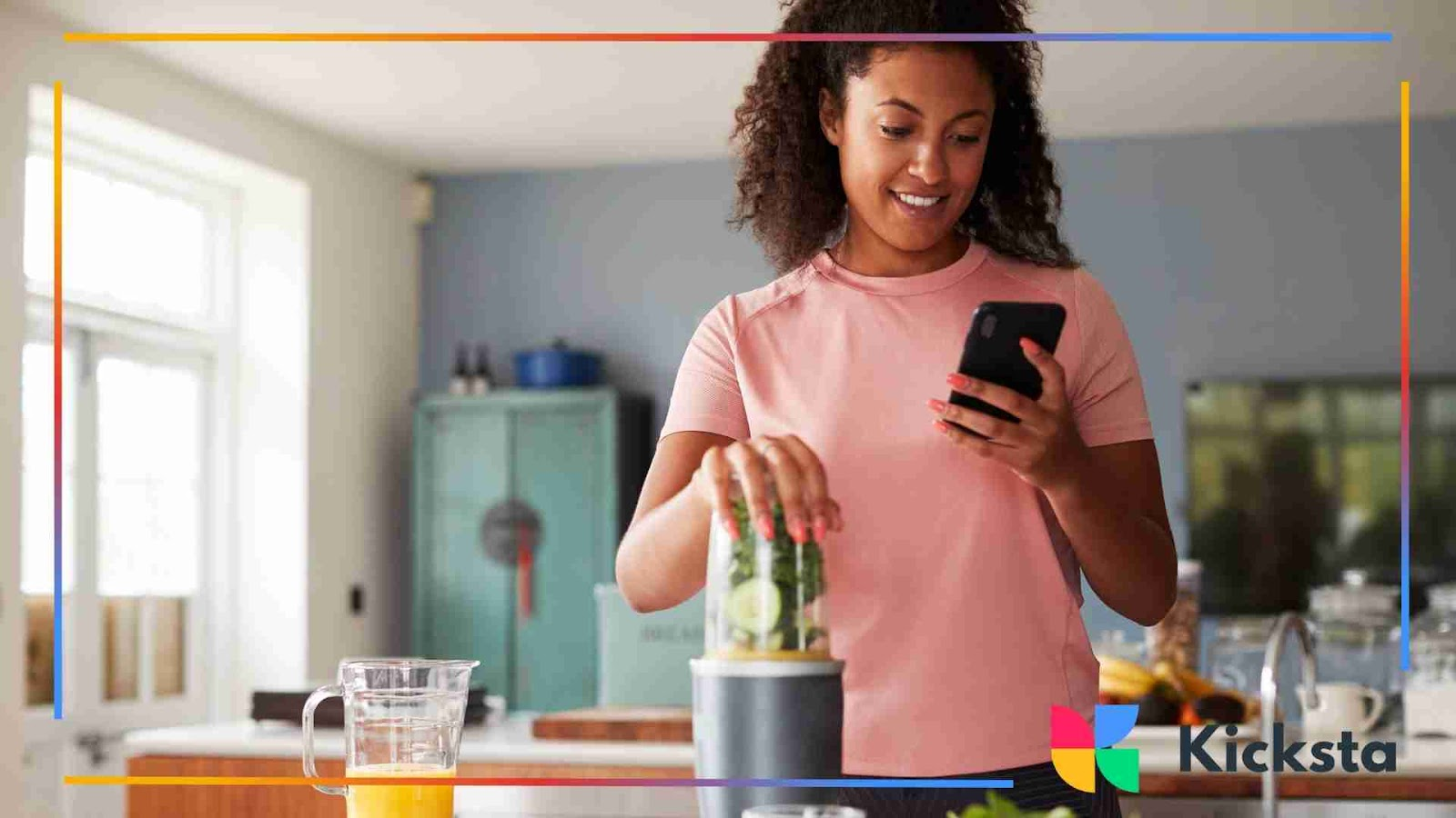 A woman blending fruits in the kitchen as she smiles at her phone.