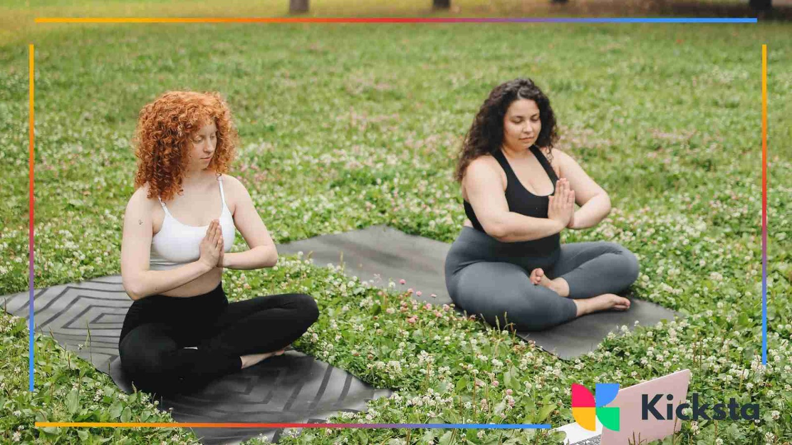 Two women practicing yoga outdoors on mats in a grassy field.