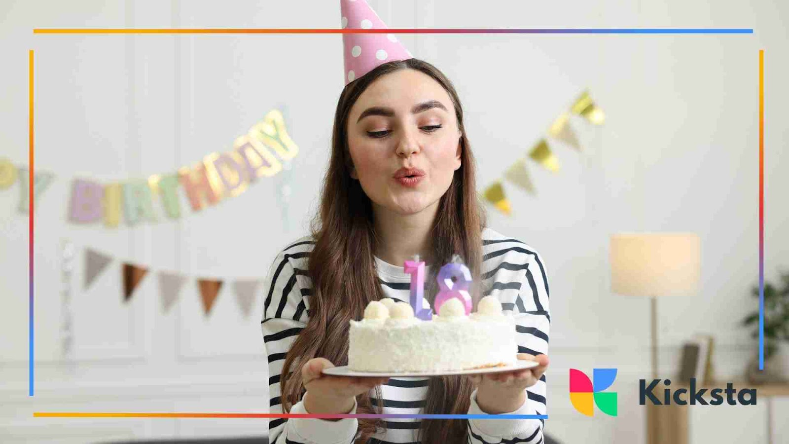 A young woman wearing a pink party hat blowing out candles on her 18th birthday cake