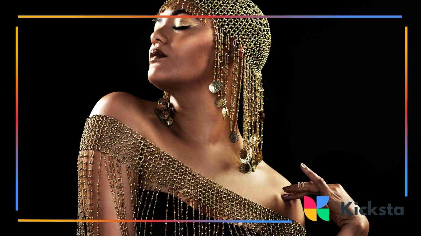 Woman dressed in a golden outfit and jewelry with a confident pose against a black background