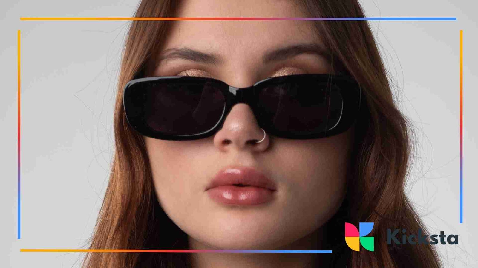 Woman with long brown hair wearing black rectangular sunglasses and a nose ring