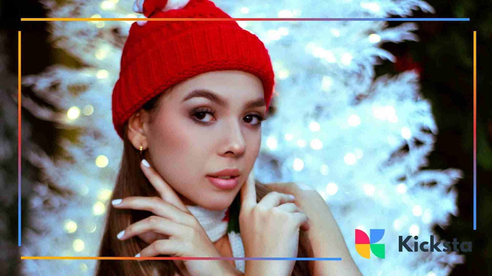 Woman wearing a red winter hat posing in front of white Christmas lights