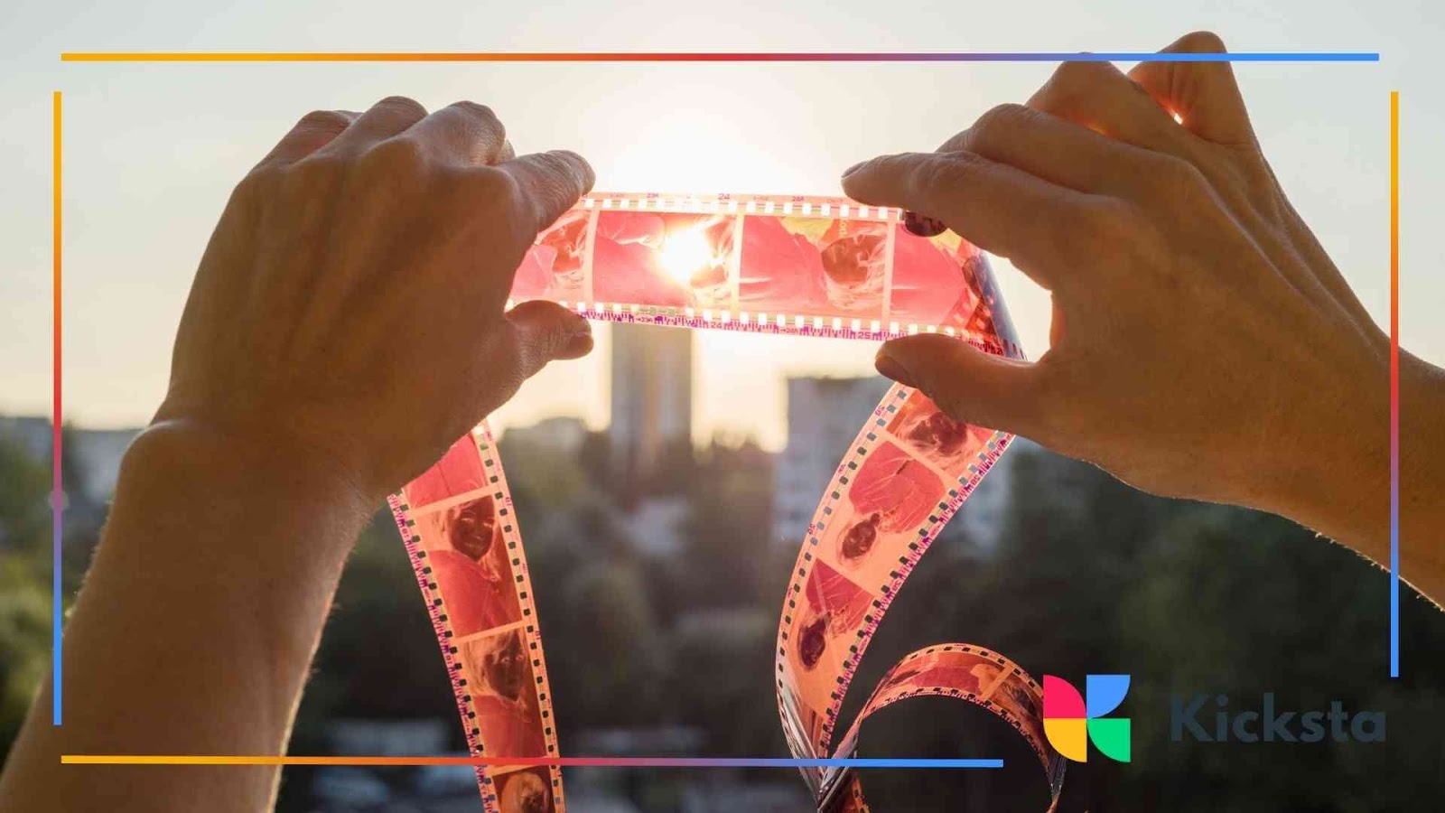 Hands holding up strips of film negatives against sunlight with a blurred city view in the background