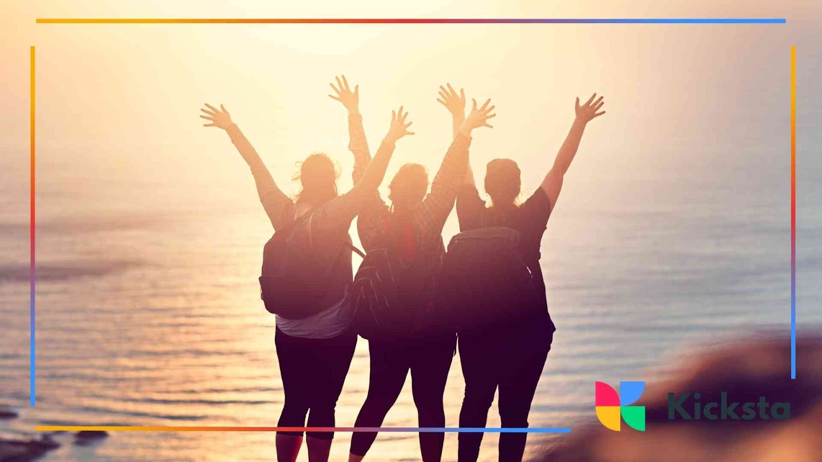 Three friends with backpacks raising their arms while watching the sunset over the ocean