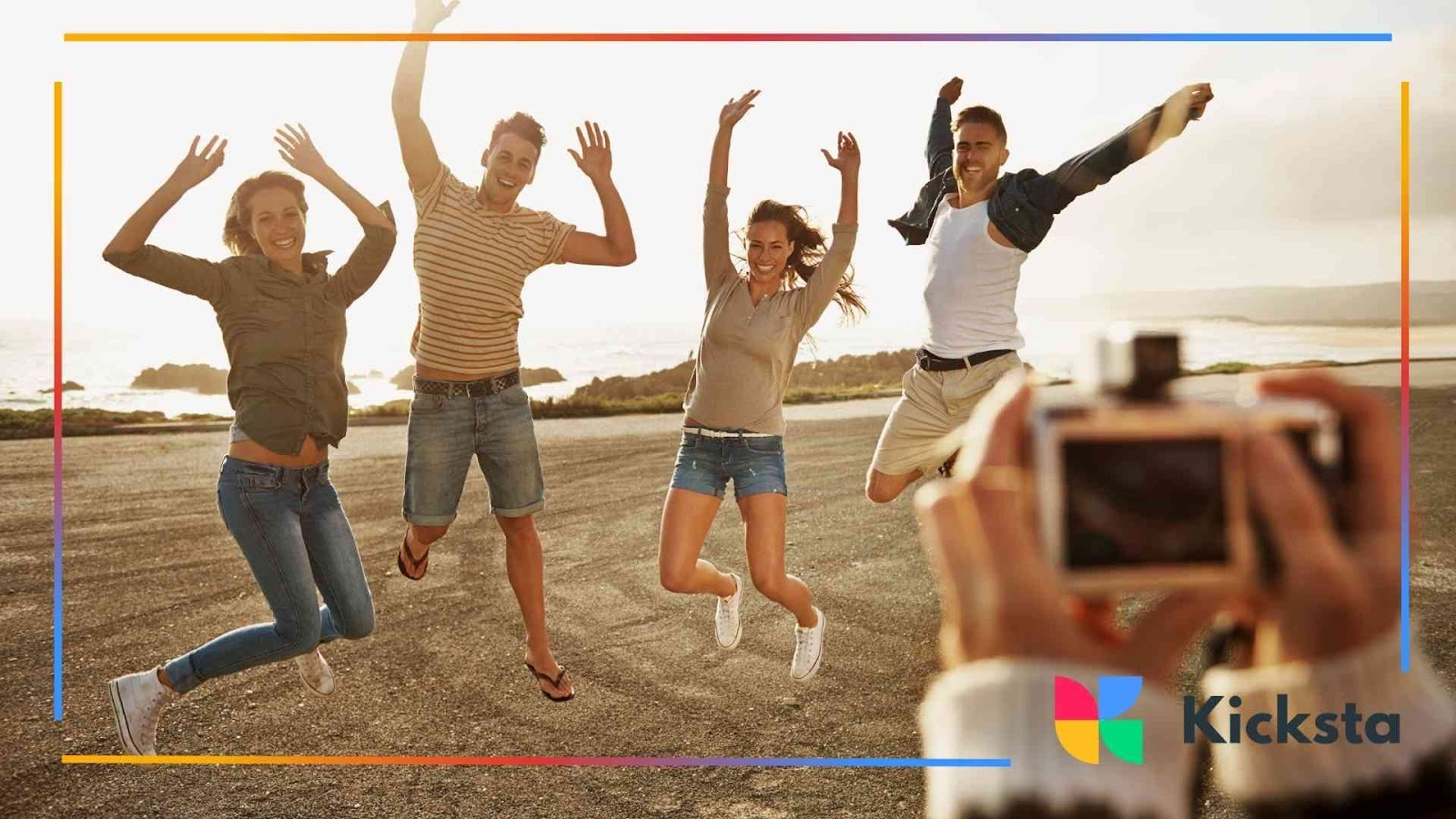 Four friends jumping joyfully on a seaside road while another person takes their photo