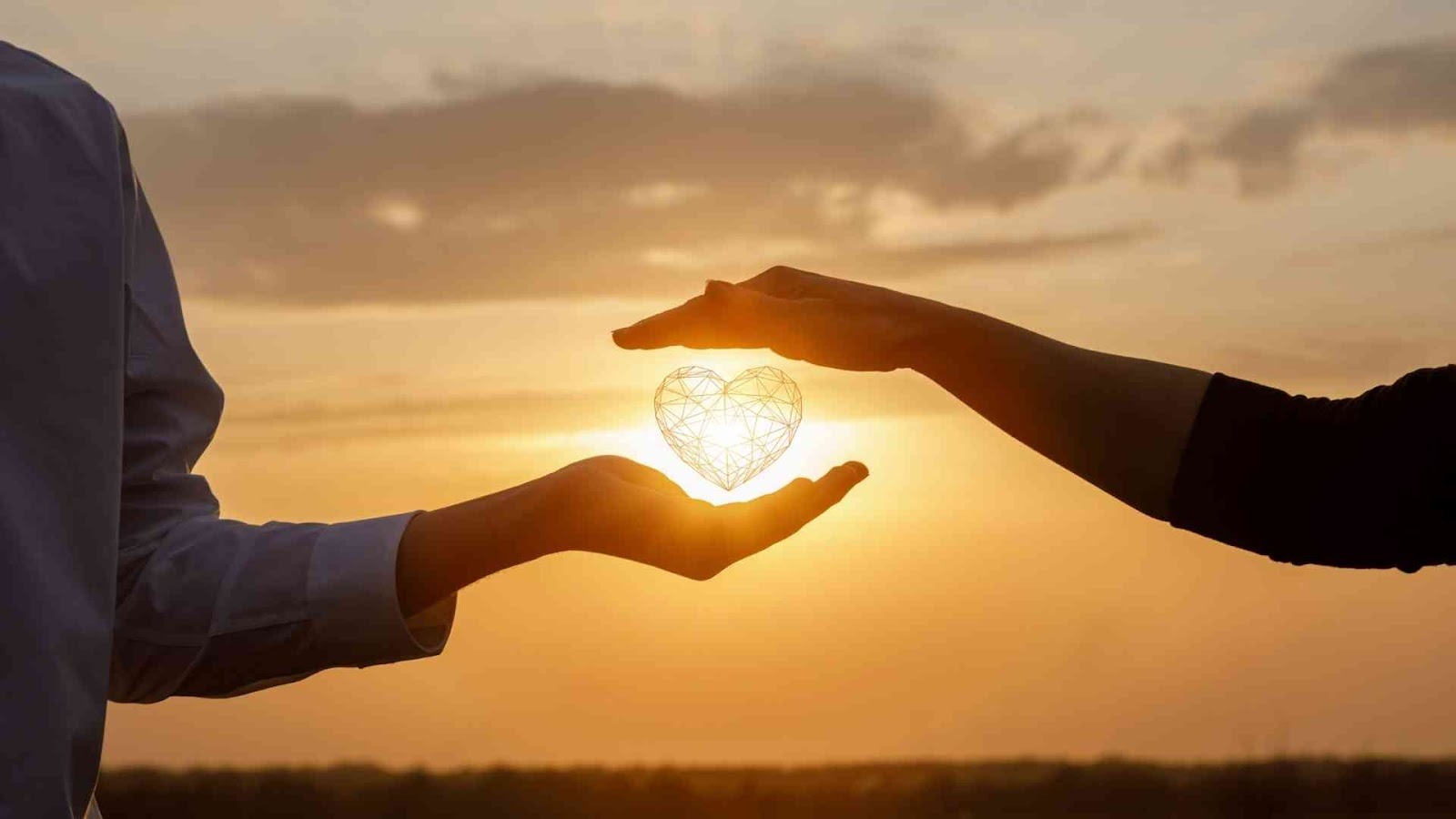 Silhouette of two hands forming and holding a wire heart shape against a golden sunset sky