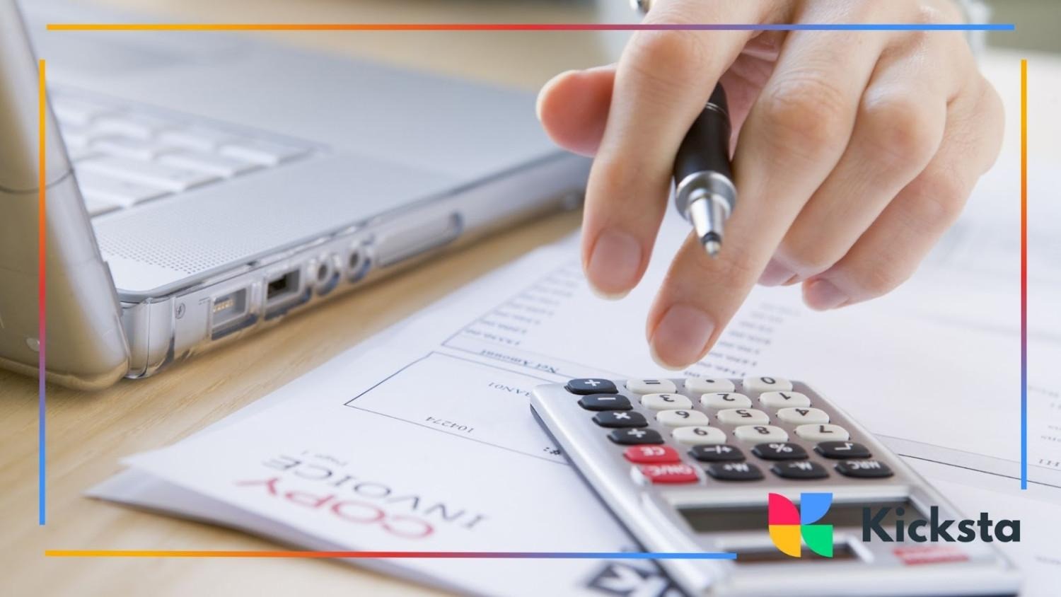 Close-up of a person using a calculator and holding a pen near a laptop and invoice documents on a desk.