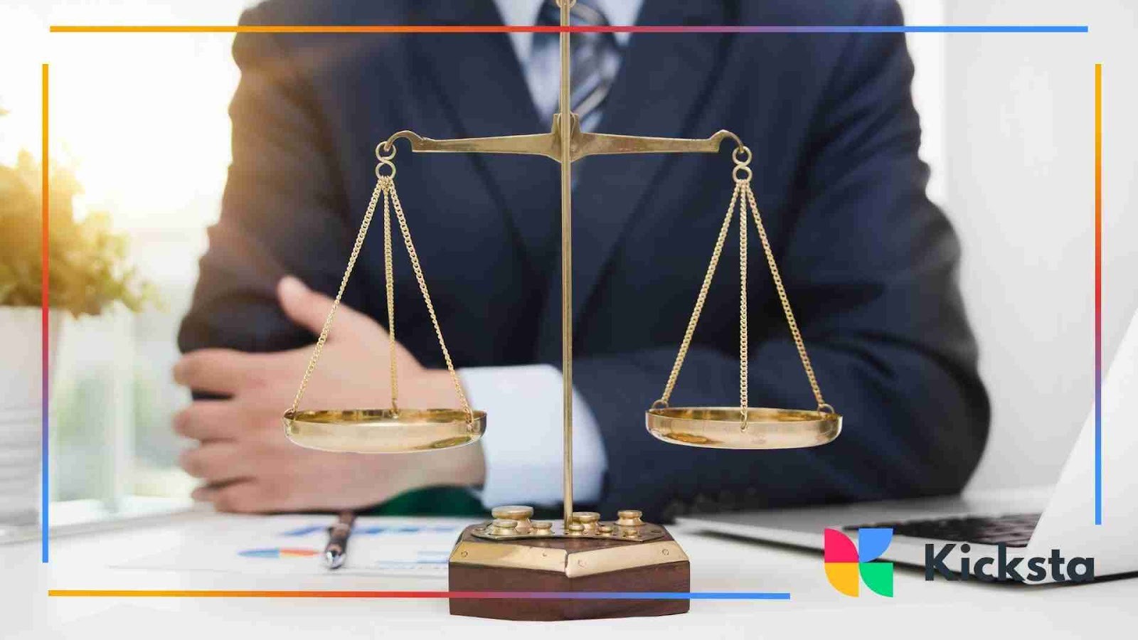 A close-up of golden scales of justice placed on a desk, with a person in a suit sitting in the background