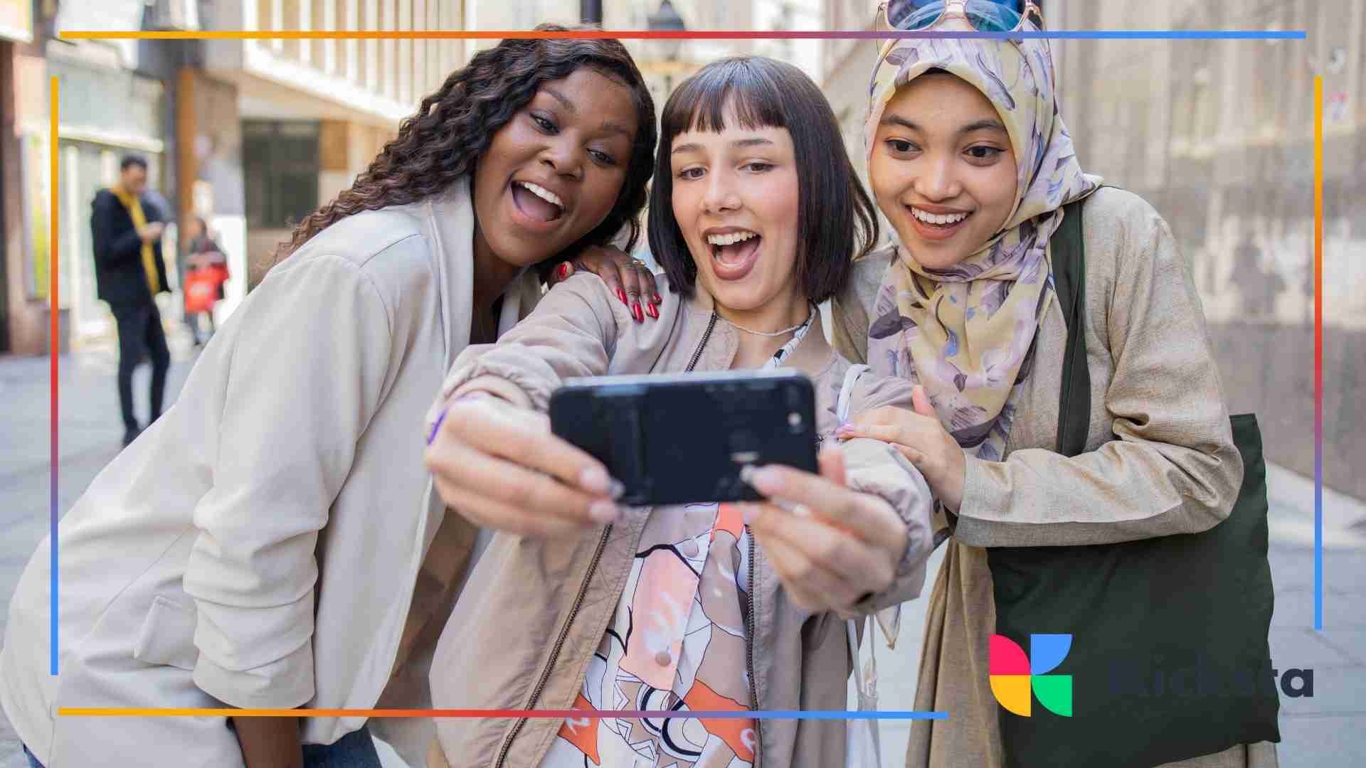 Three friends smiling and taking a selfie on the street.
