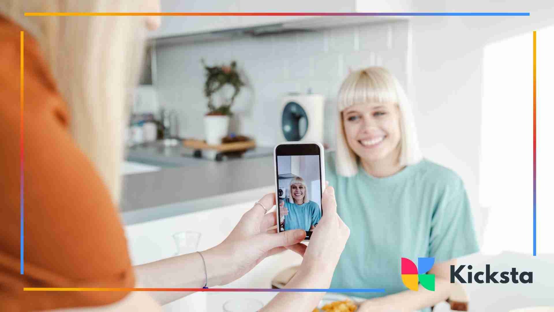 Person taking a photo of a woman smiling in a kitchen setting.