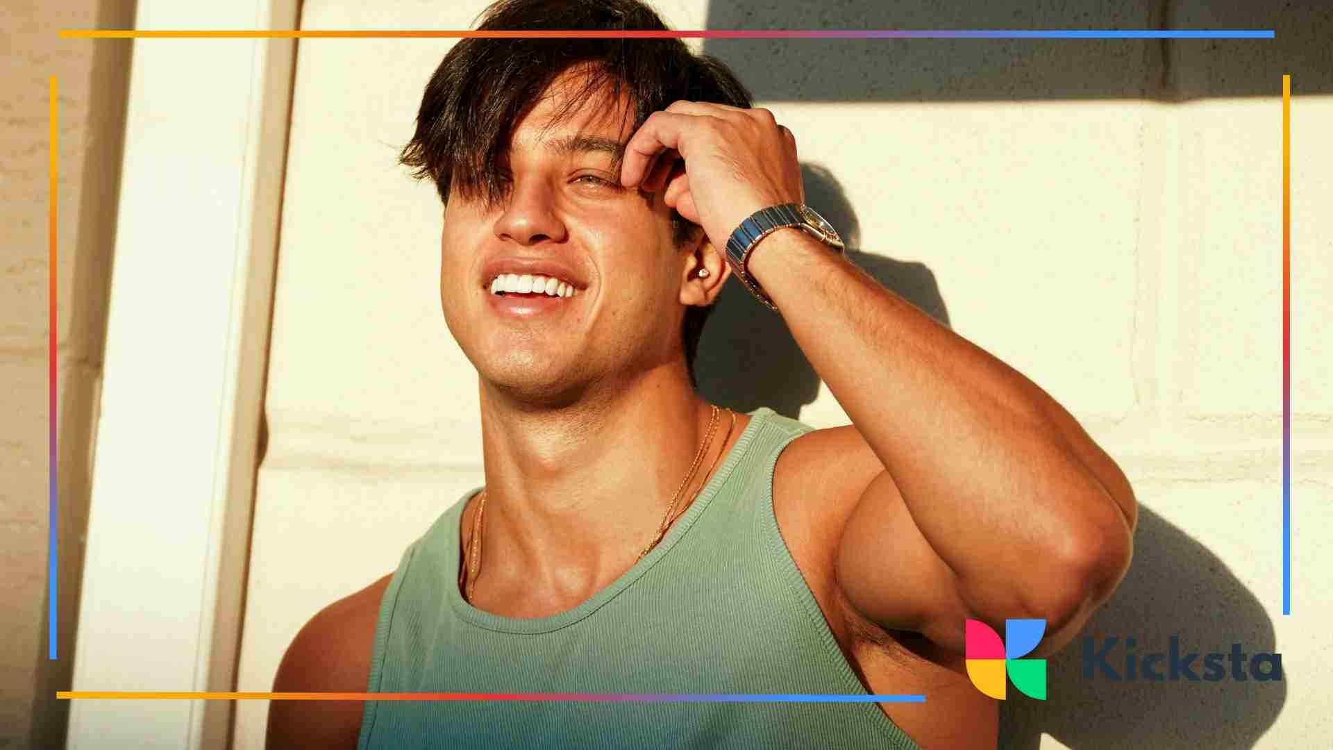 Smiling man in a green tank top touching his hair in bright sunlight.