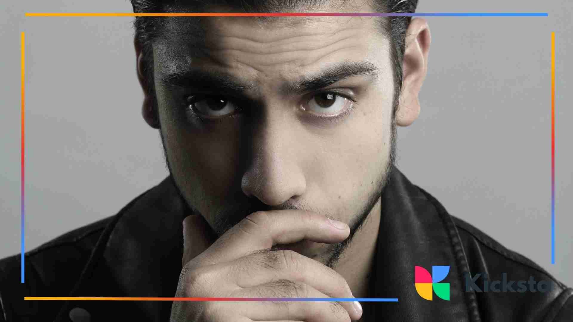 Close-up of a man in a leather jacket resting his hand near his mouth.