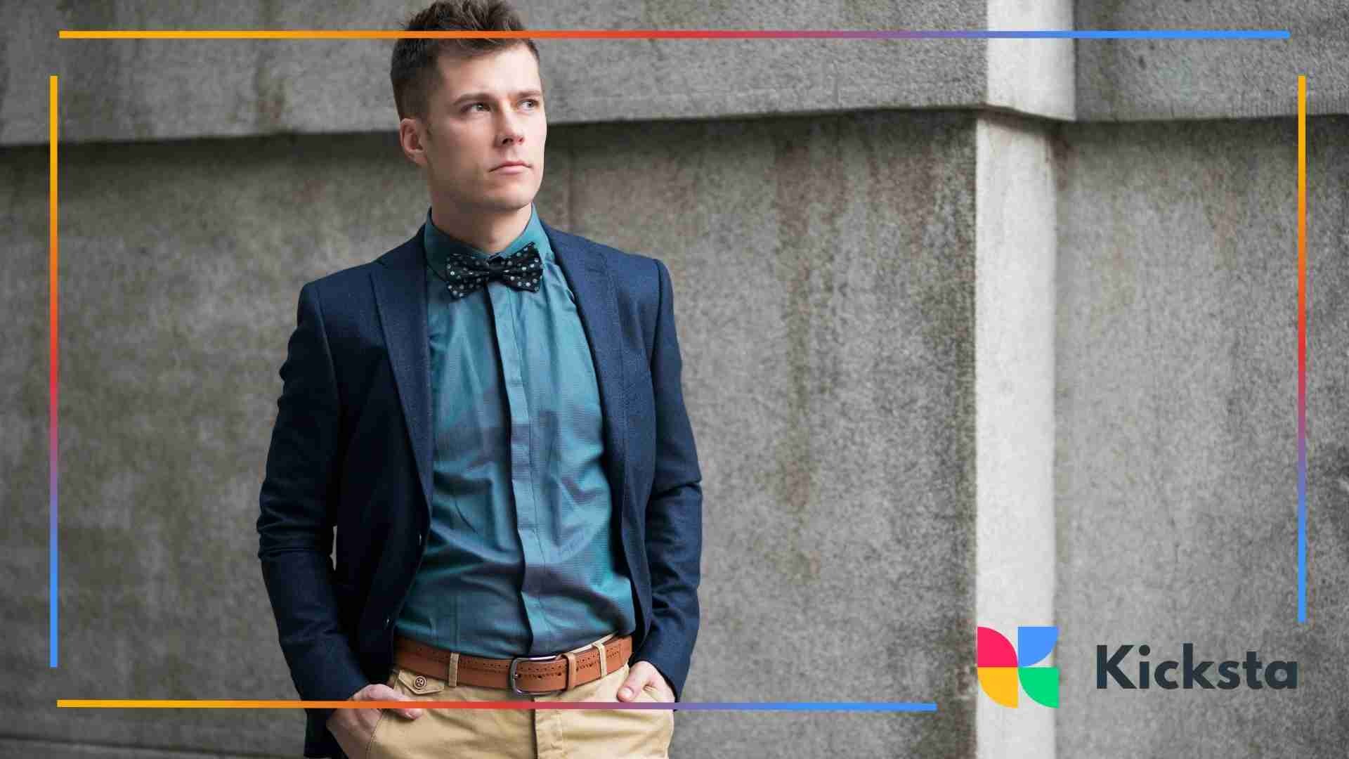 Man in a navy blazer and bow tie posing against a concrete wall.