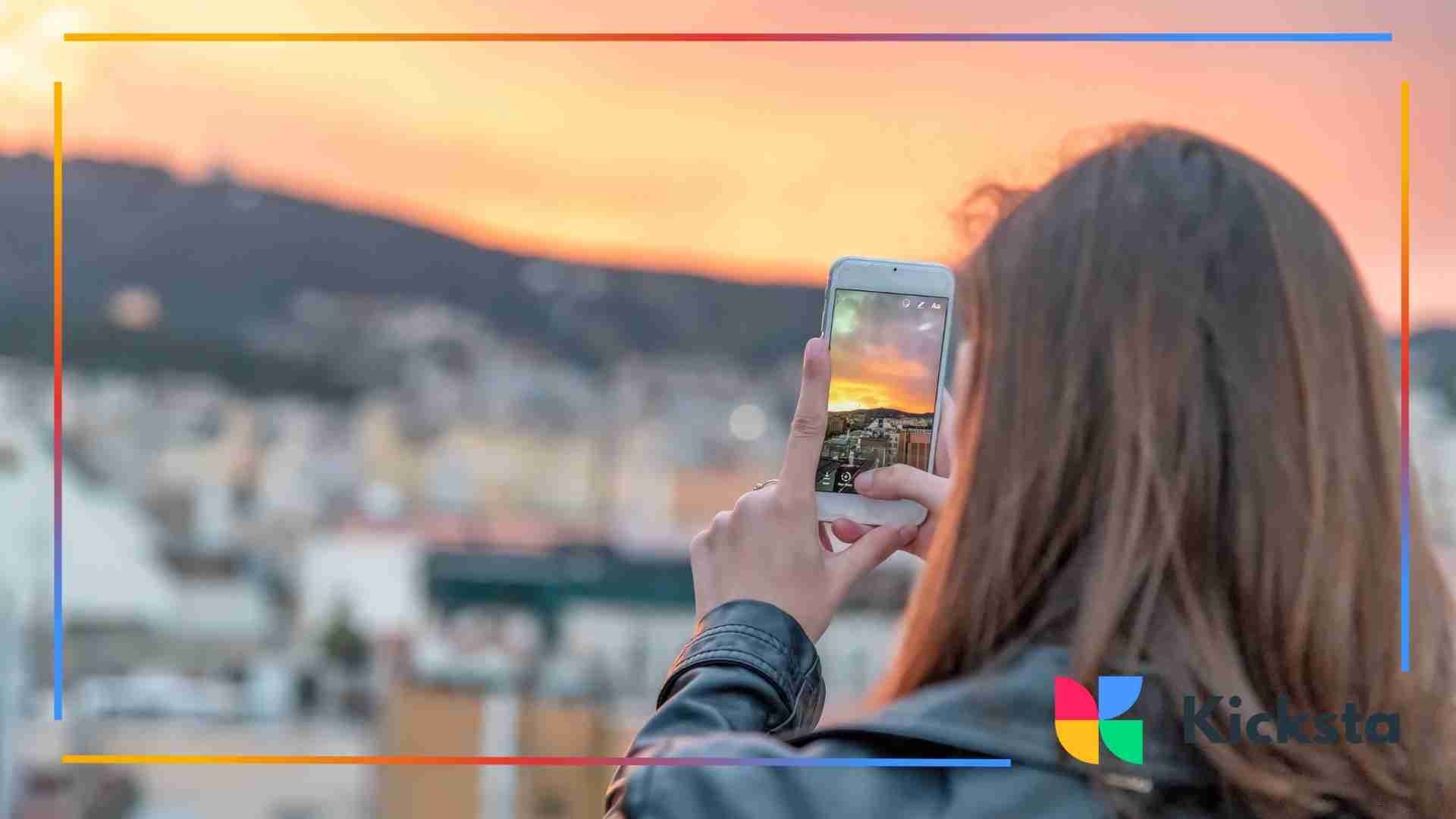 Woman photographing a cityscape at sunset with her smartphone.