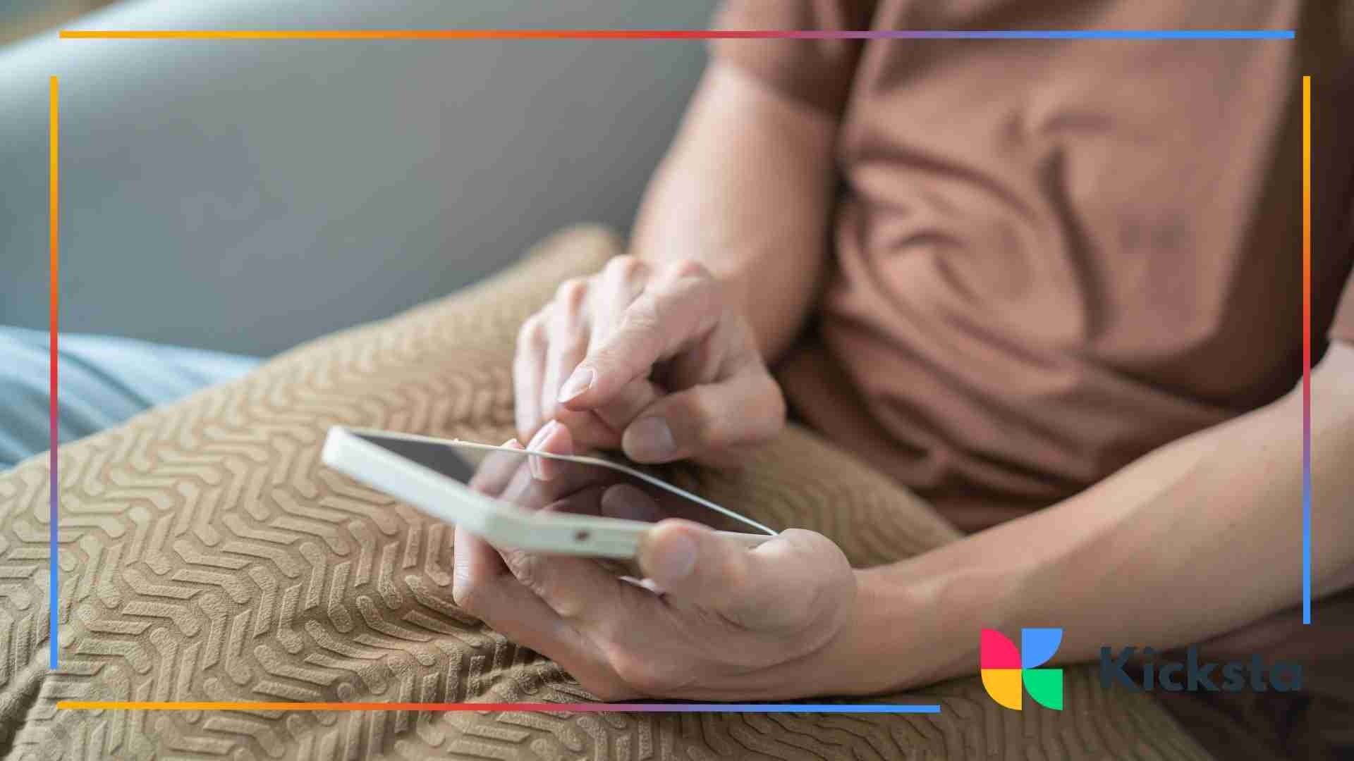 Person sitting on a couch using a smartphone with one hand while resting on a patterned cushion.