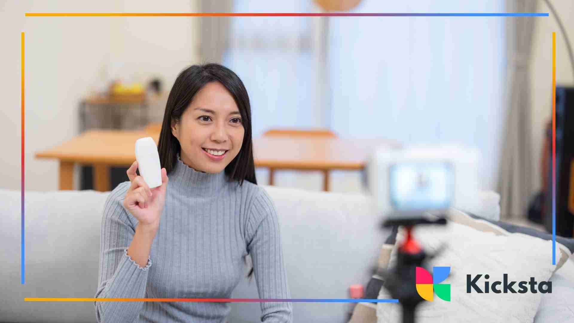 Woman filming a product review while holding a small white item in front of a camera.