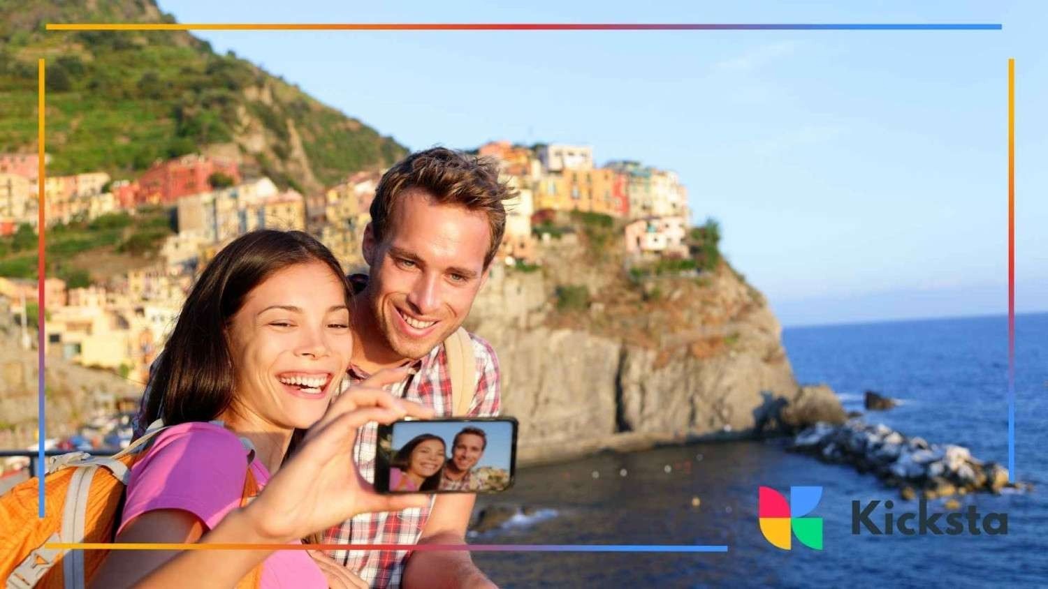 Happy couple taking selfie with smartphone near coastal town and ocean, representing travel influencers, vacation photography, and social media content.