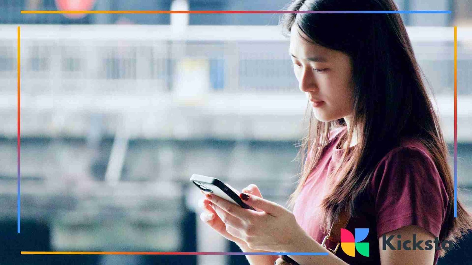 A young woman standing outside and focused on her smartphone, holding it with both hands.