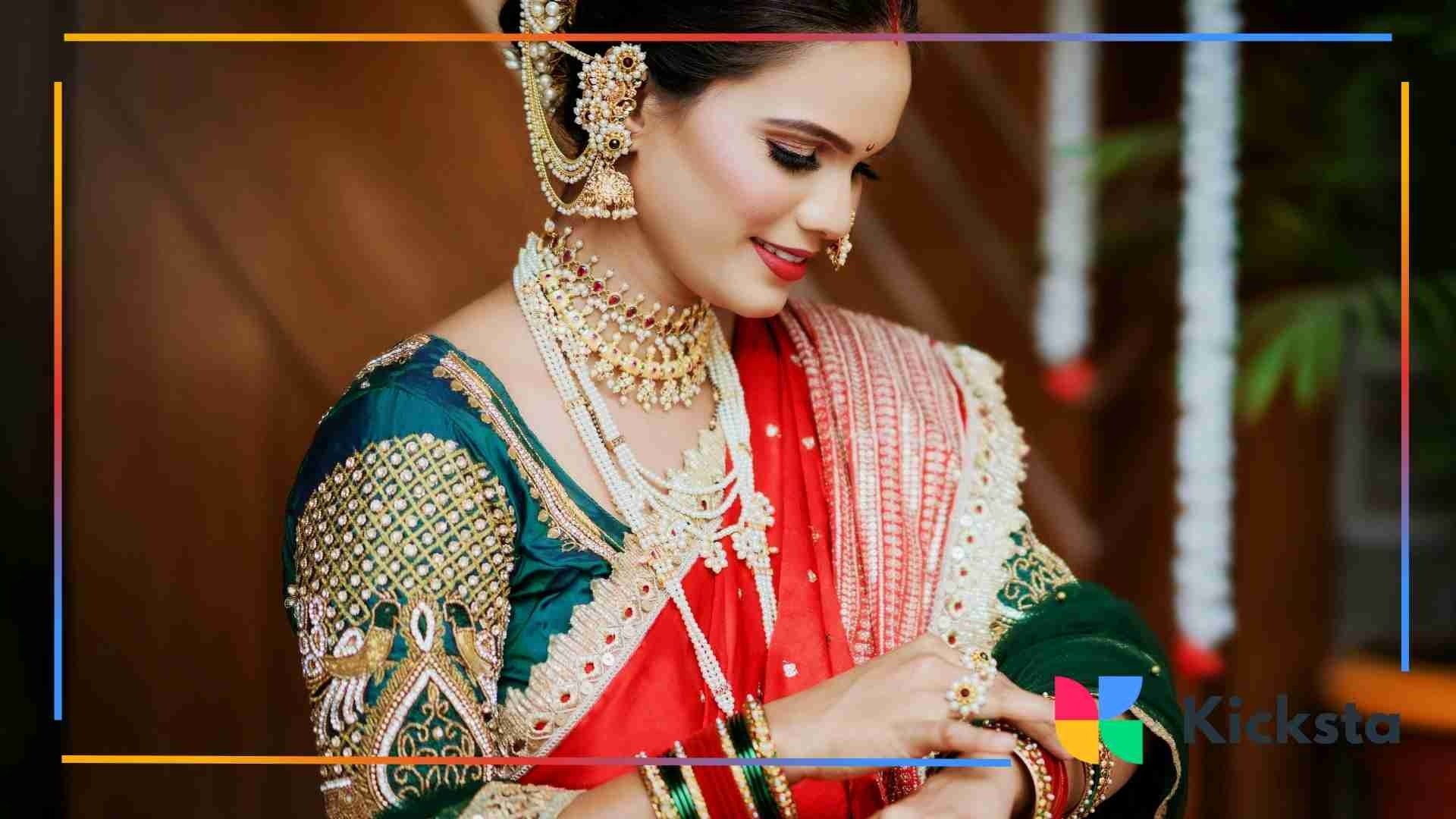 A bride wearing a green and red traditional saree with heavy gold jewelry smiles as she adjusts her bangles.