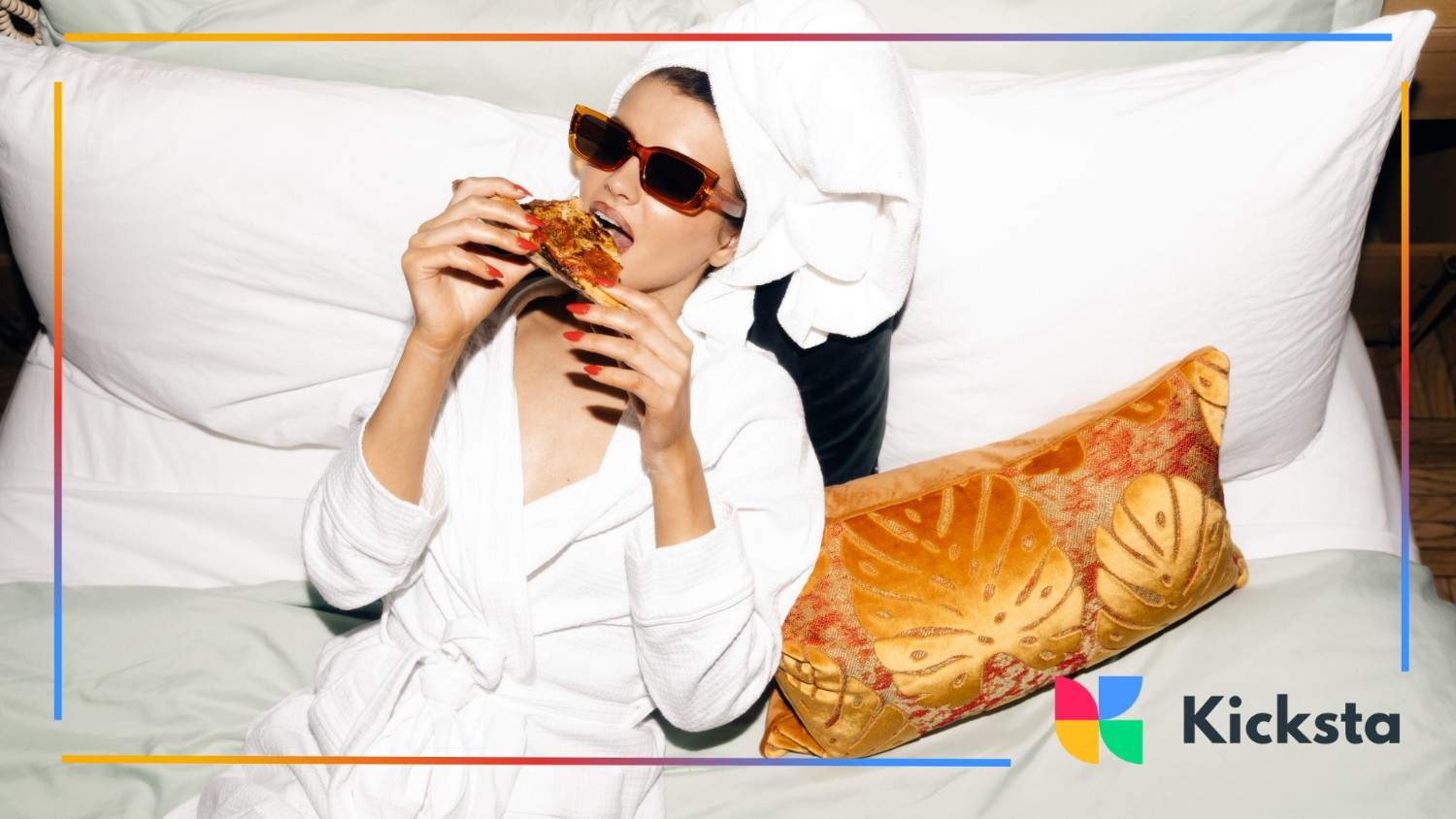 Stylish woman in sunglasses and bathrobe enjoying pizza while lounging on a bed.