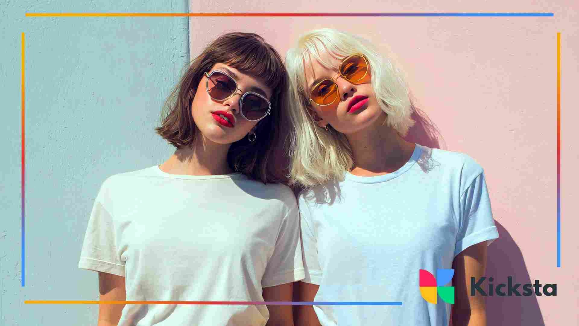 Two fashionable young women wearing sunglasses and white T-shirts posing together against a pastel pink and blue wall.
