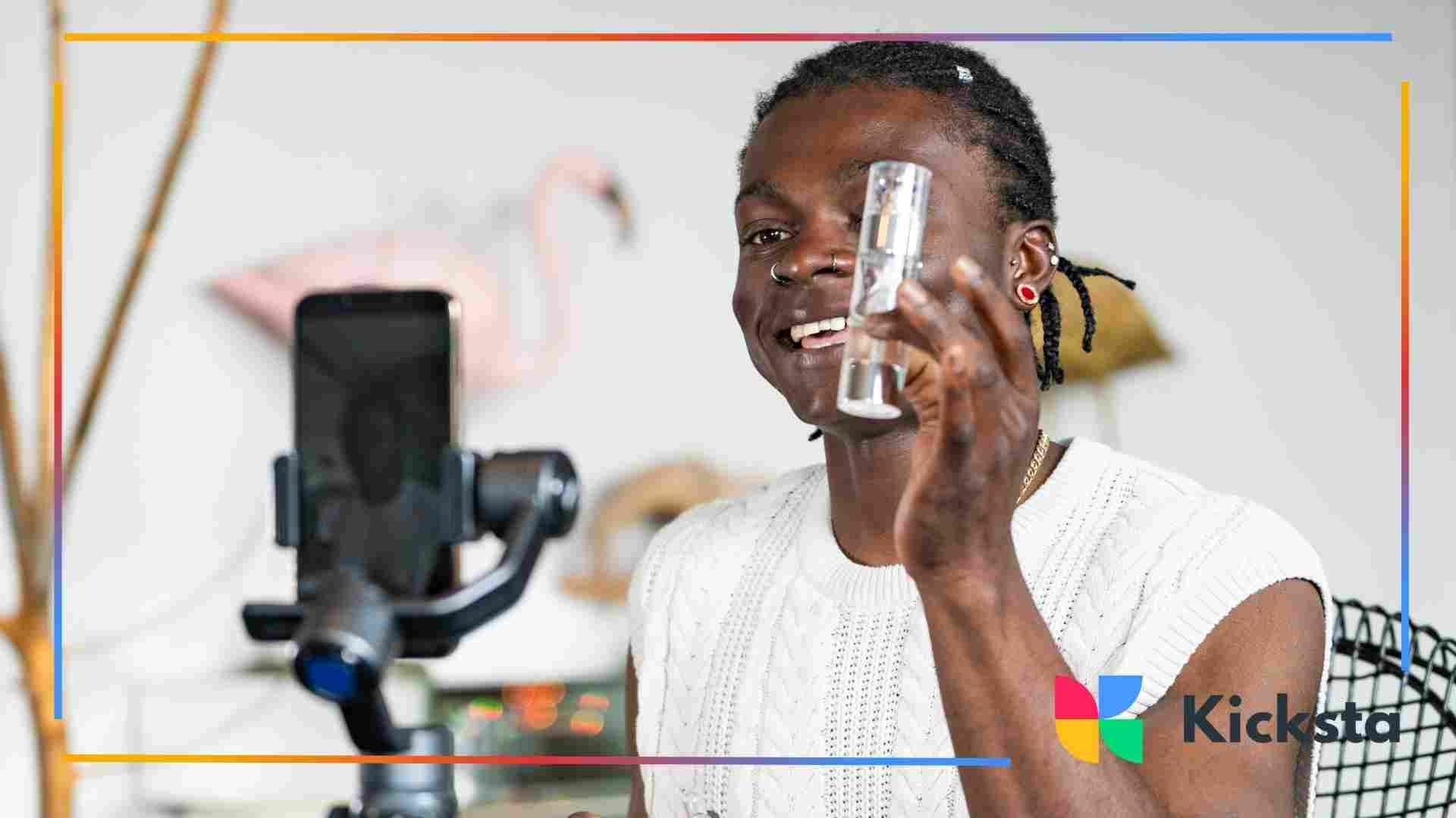 Smiling man holding up a skincare bottle while recording himself with a smartphone on a stabilizer in a home studio.