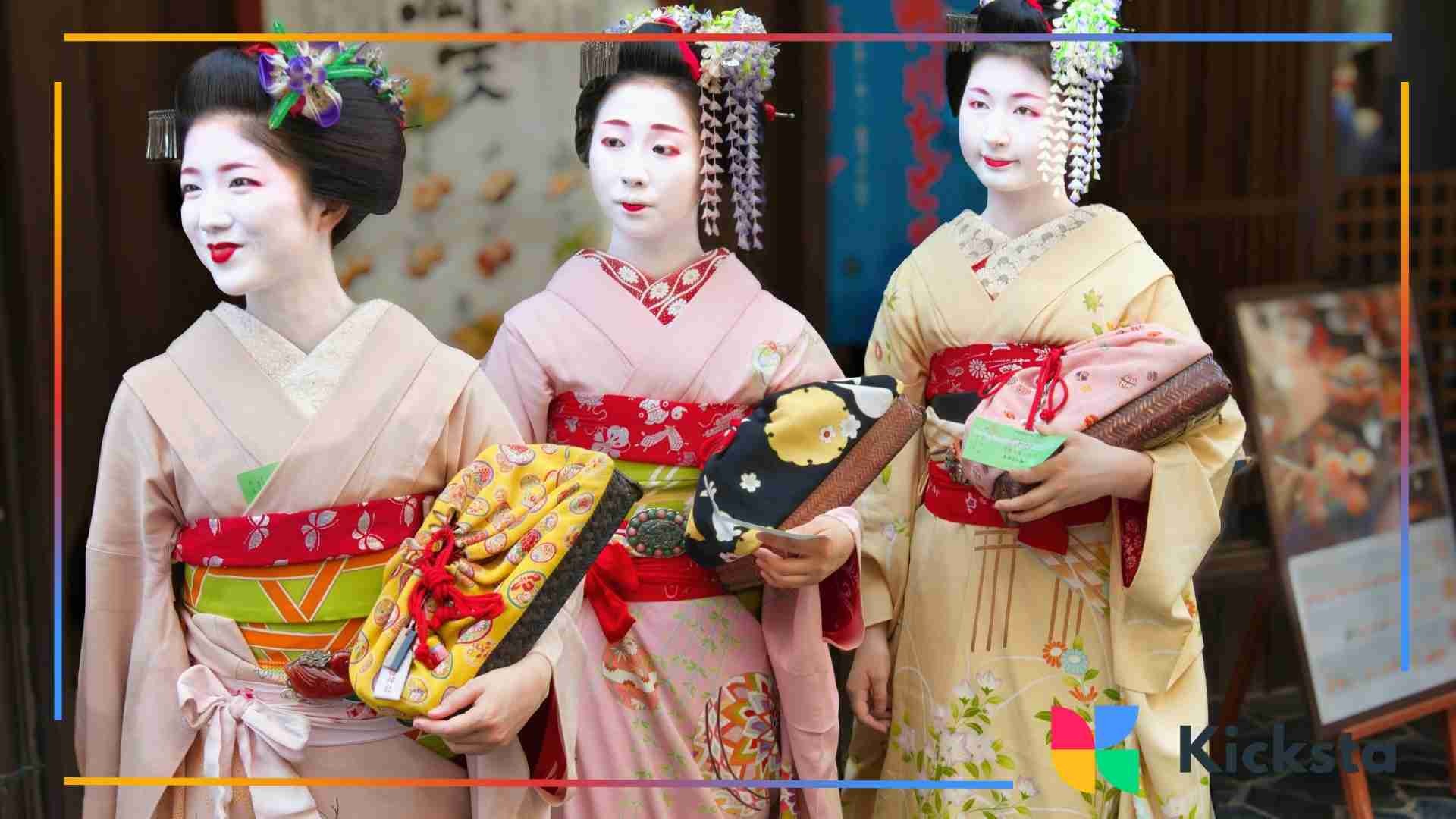Three women dressed in traditional geisha-style kimono with white face makeup, red and floral accessories, and intricately styled hair, standing together.